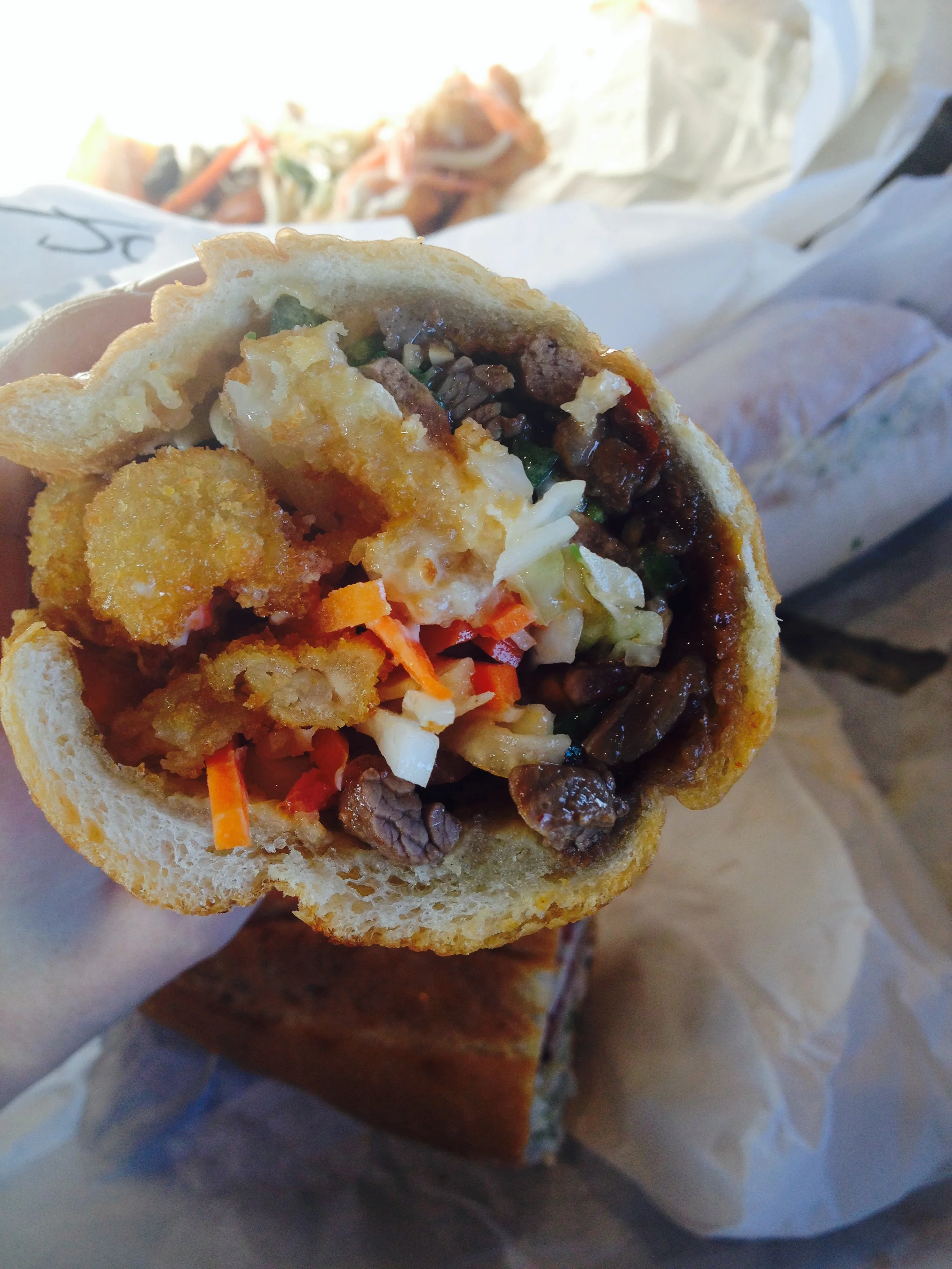 The FAT BANH MI-KI, with sweet & spicy soy marinated grilled steak, vietnamese pickled vegetables, szechuan slaw, onion rings, tomato, fresh jalapeños, cilantro, teriyaki glaze, sriracha, mayo, served on a garlic hero.