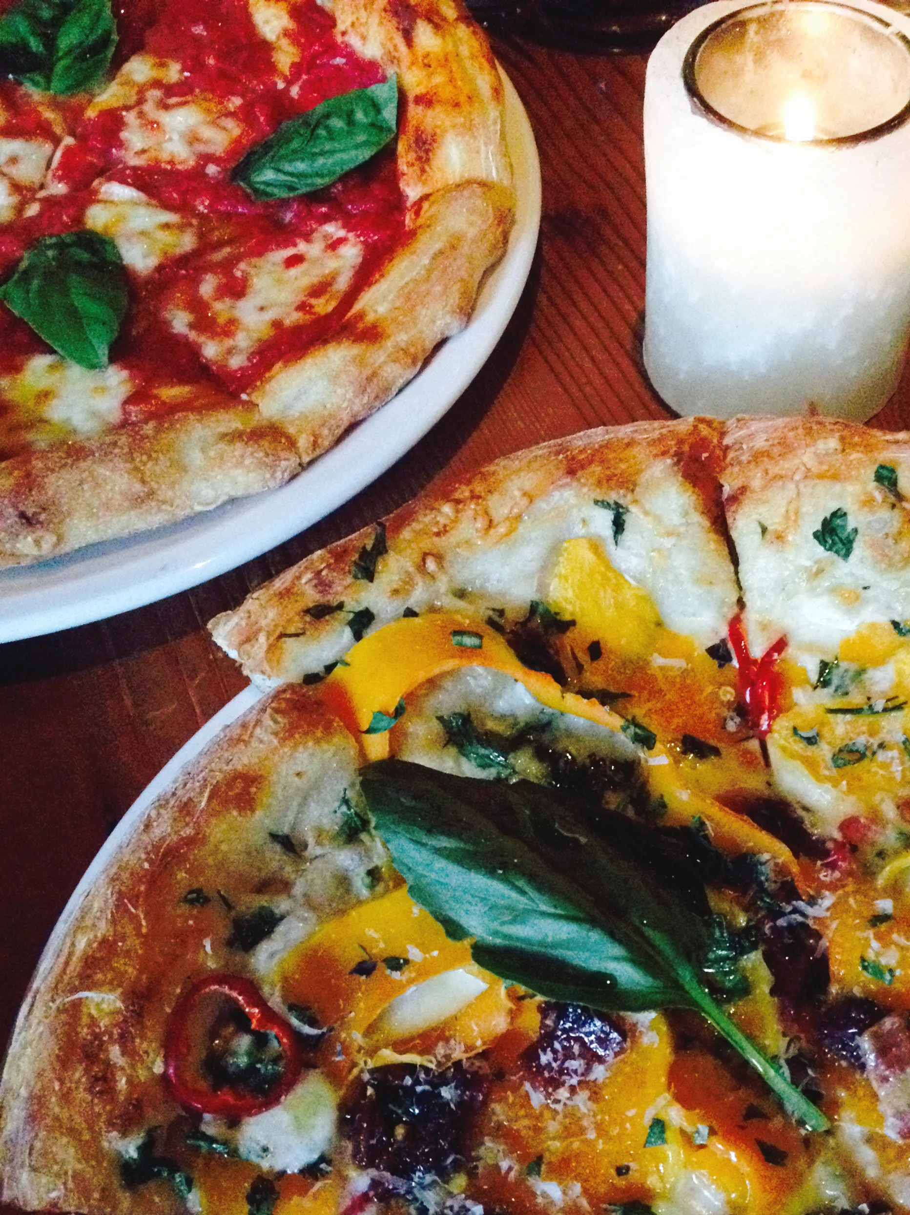 (Foreground) Butternut Squash Pizza with candied bacon, taleggio cheese, fresno chili, oregano, parsley, and parmesan. (Background) Margherita Pizza with fresh mozzarella, basil, and organic extra virgin olive oil.