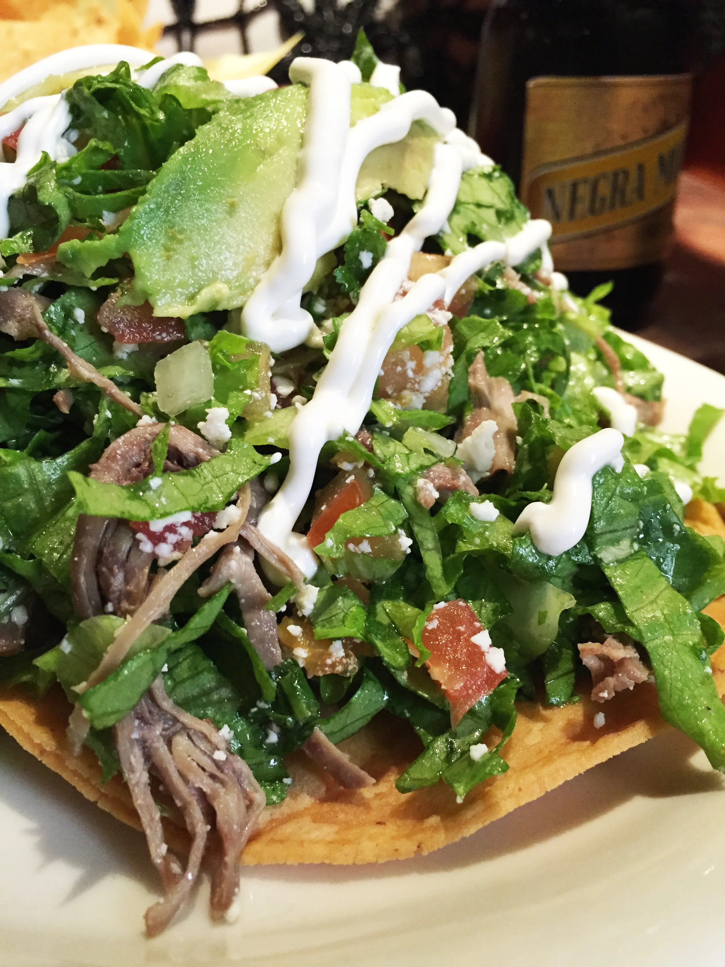 Salpicon Tostada with cold shredded beef, beans, lettuce, cotija cheese, pico de gallo, sour cream, and avocado on two corn tortilla shells.