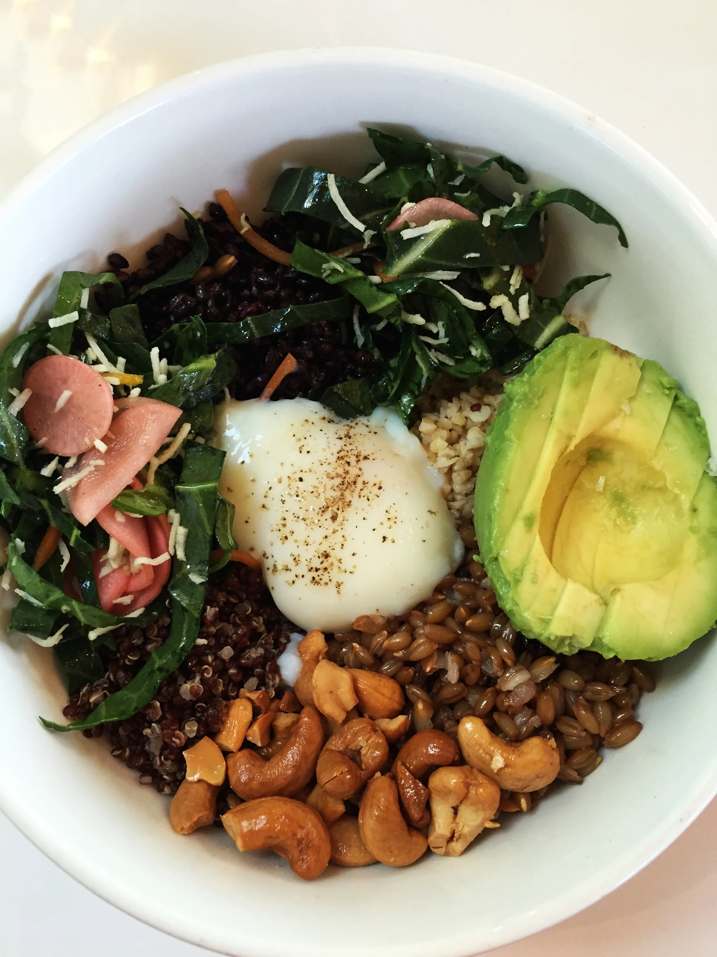 Grain Bowl with runny egg, pickles, collard slaw, cashews, and avocado.