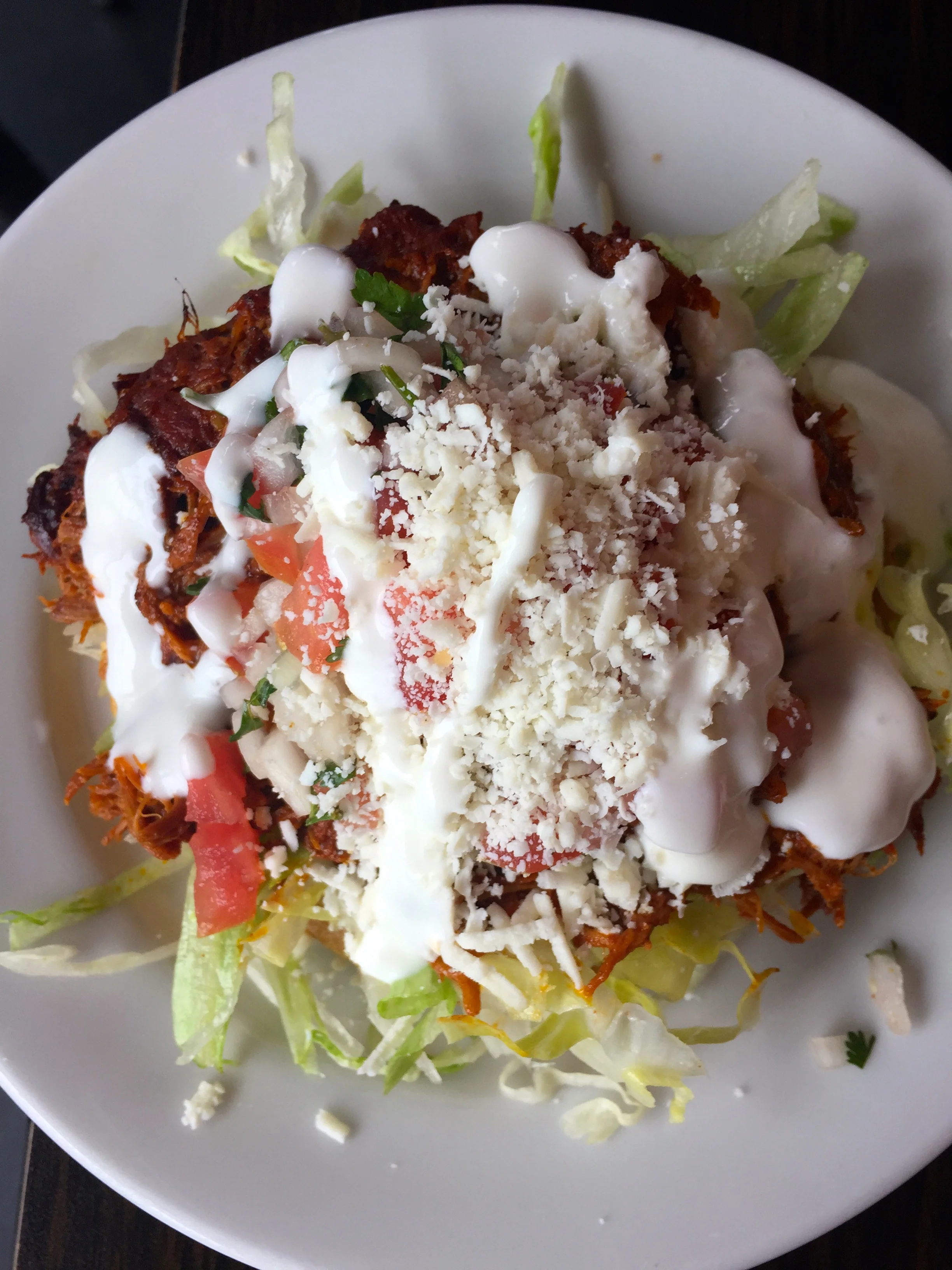 Yucatan-spiced shredded pork Cochinita Pibil Sope, with lettuce, crema, and queso fresco.