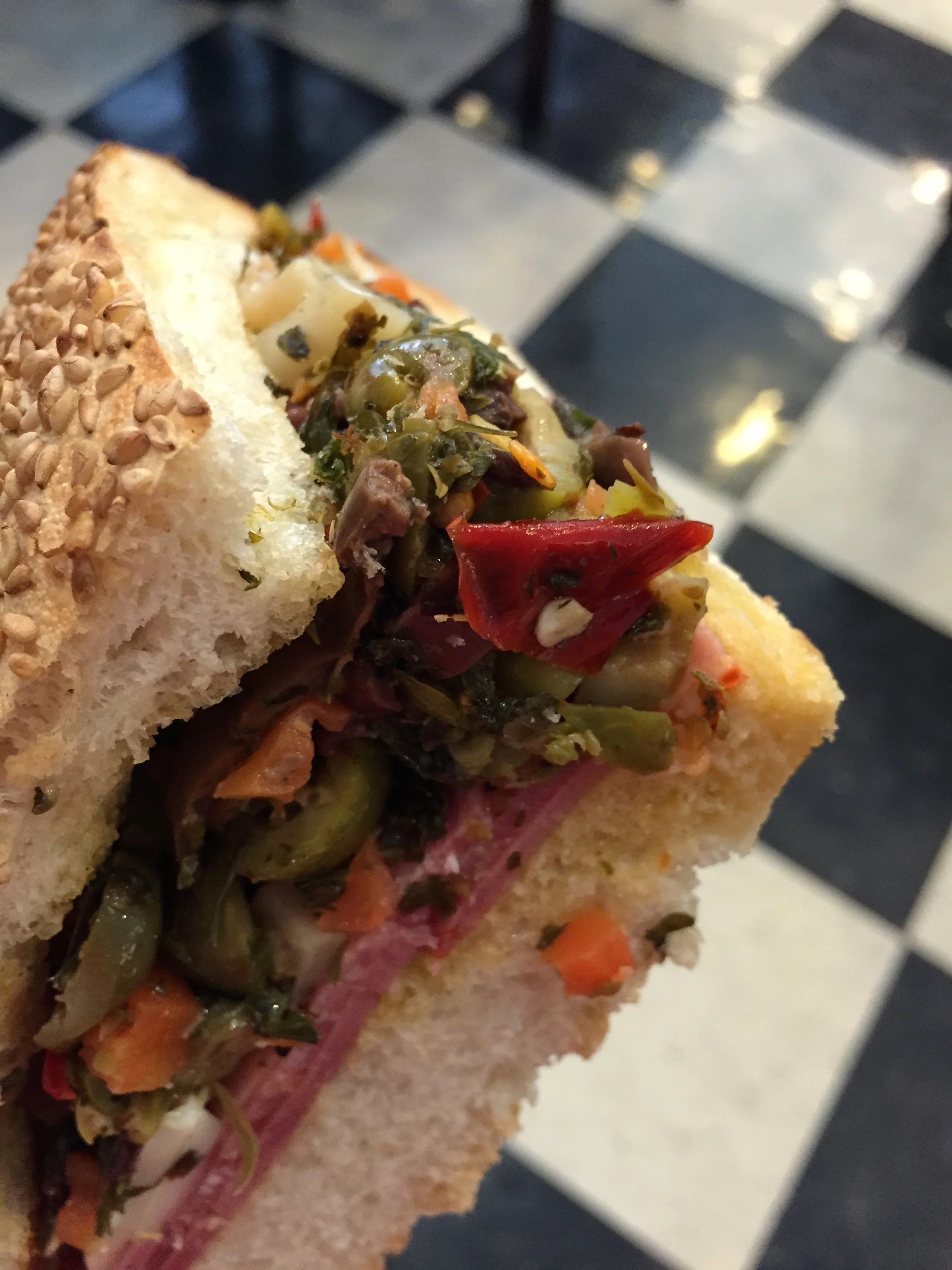 Muffuletta - New Orleans Sicilian sandwich consisting of Genoa Salami, Soppressata, Hot Capicola, and Mortadella meats, Provolone and Mozzarella cheeses, and House-Made Olive Salad on a sesame seeded Leidenheimer loaf.