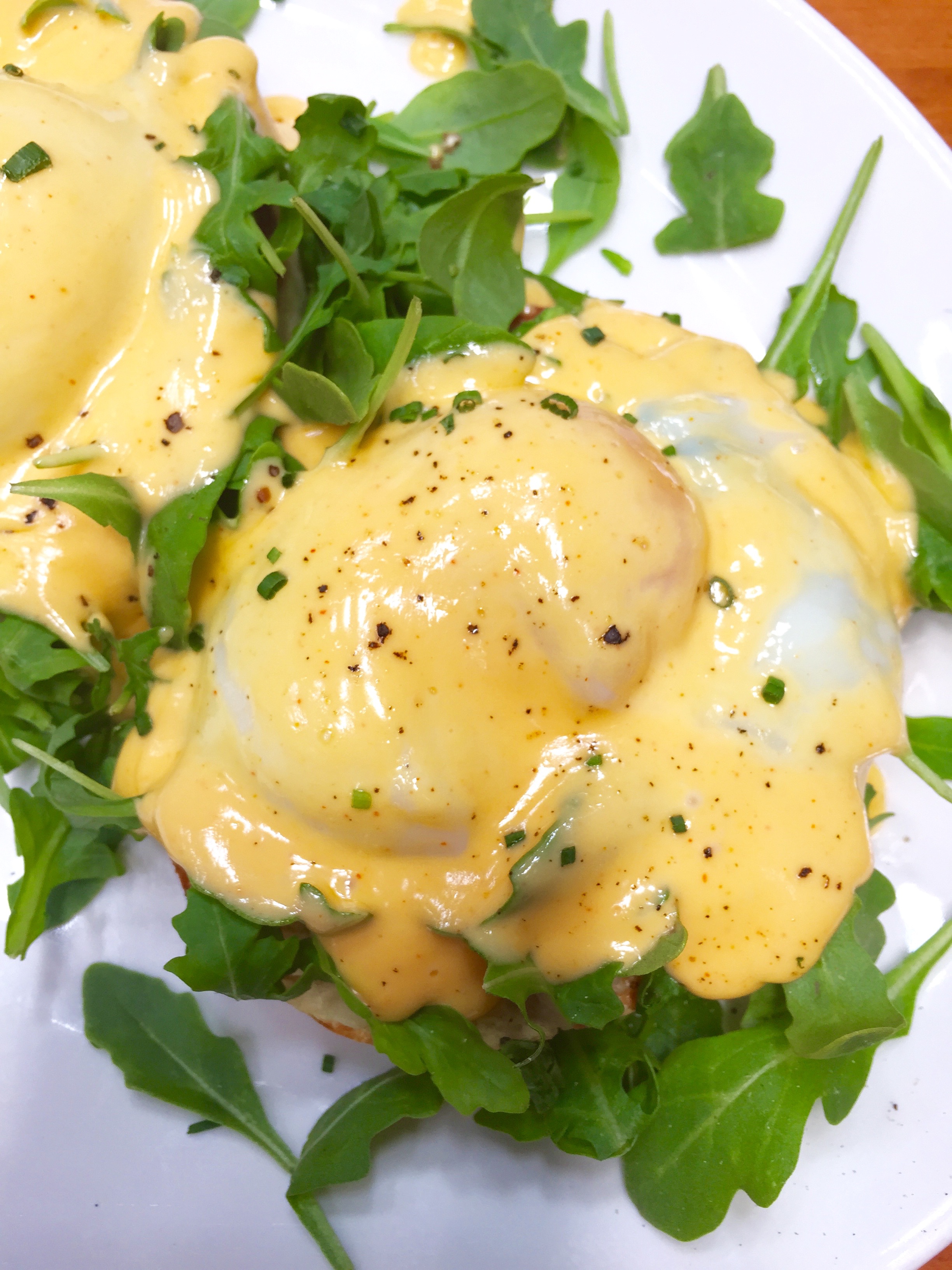 Eggs Benedict with Canadian bacon, arugula, slow poached eggs, hollandaise, and English muffin.