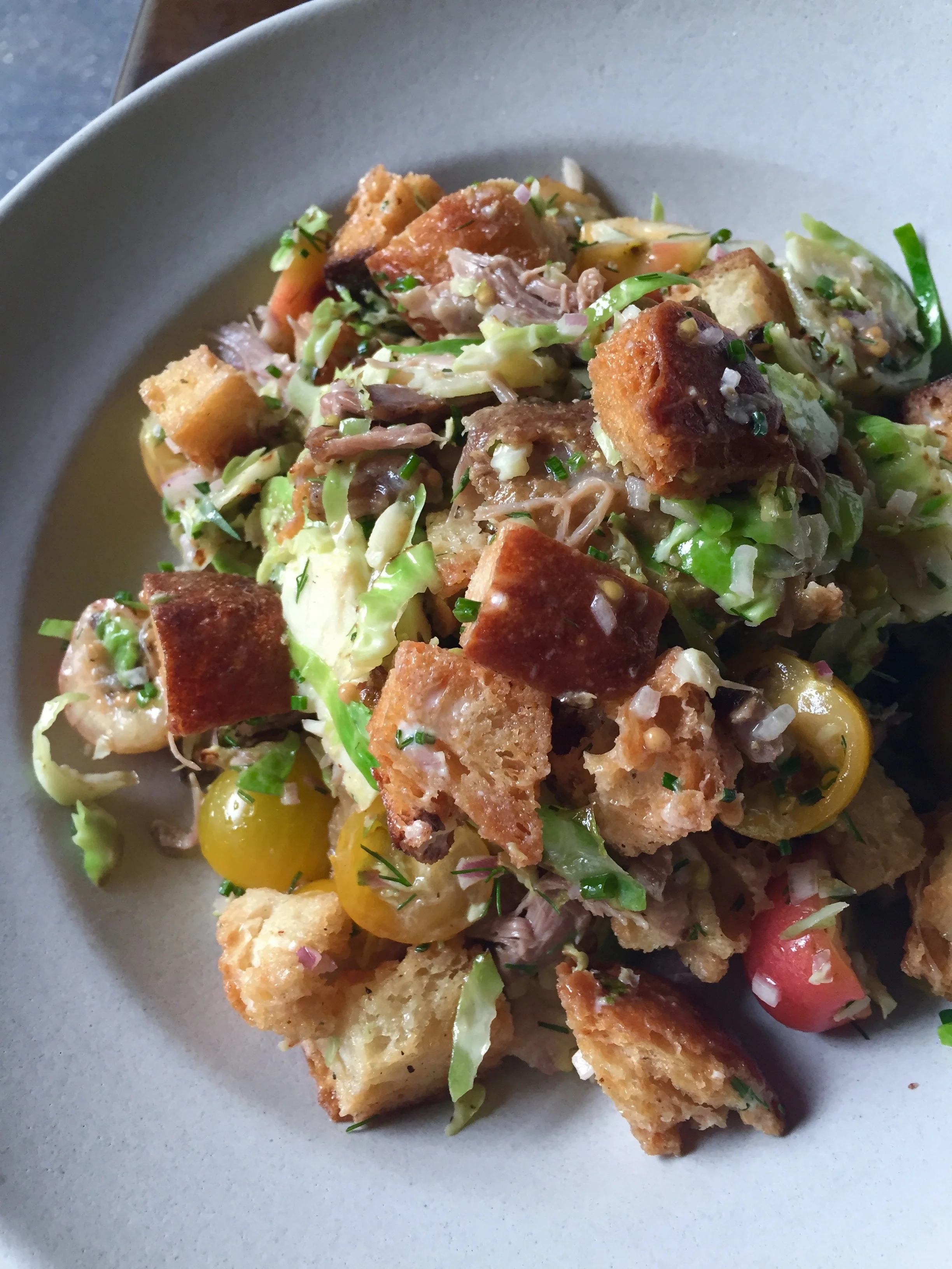 Confit Duck & Shaved Brussels Sprouts Salad with cherries, tomatoes, croutons, and blue cheese.