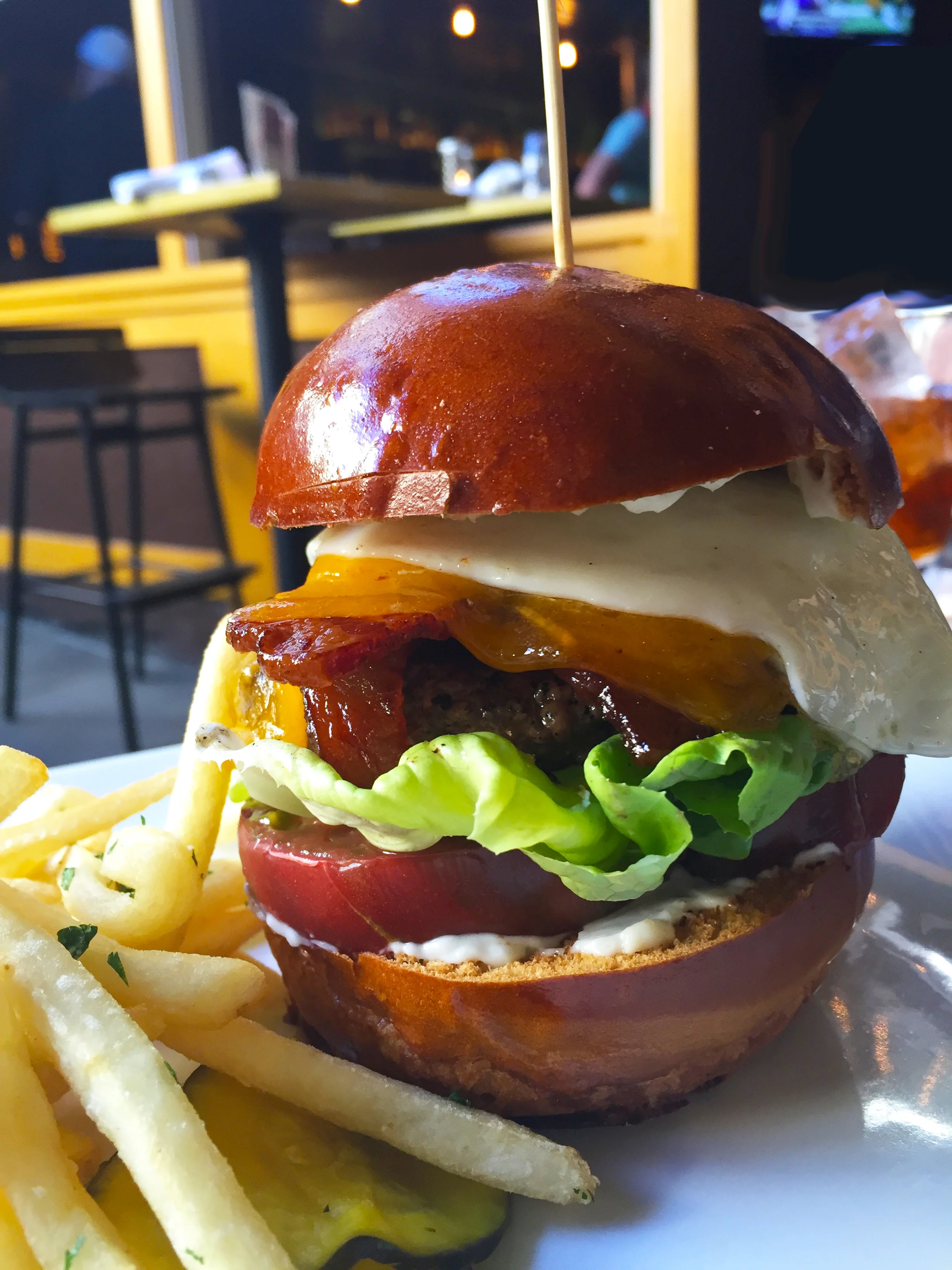 Hangover Burger with 100% all natural in-house grind, brioche bun, lettuce, tomato, aioli and sharp cheddar with bacon and a fried egg.