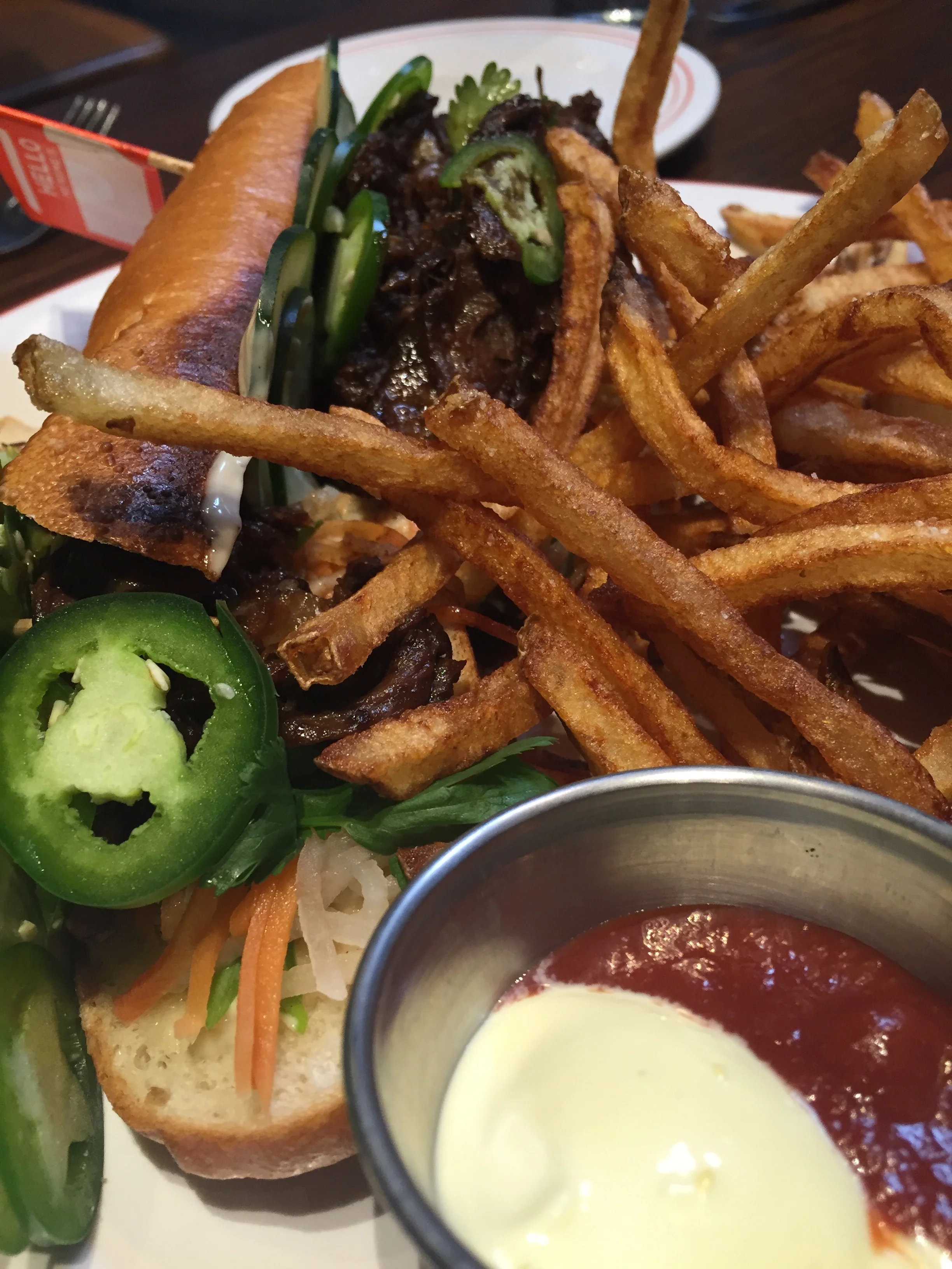Braised Short Rib Sandwich - beef short ribs braised in coconut milk, pickled carrot & daikon, cucumbers, scallions, cilantro, jalapeños, & roasted garlic mayo with fries.