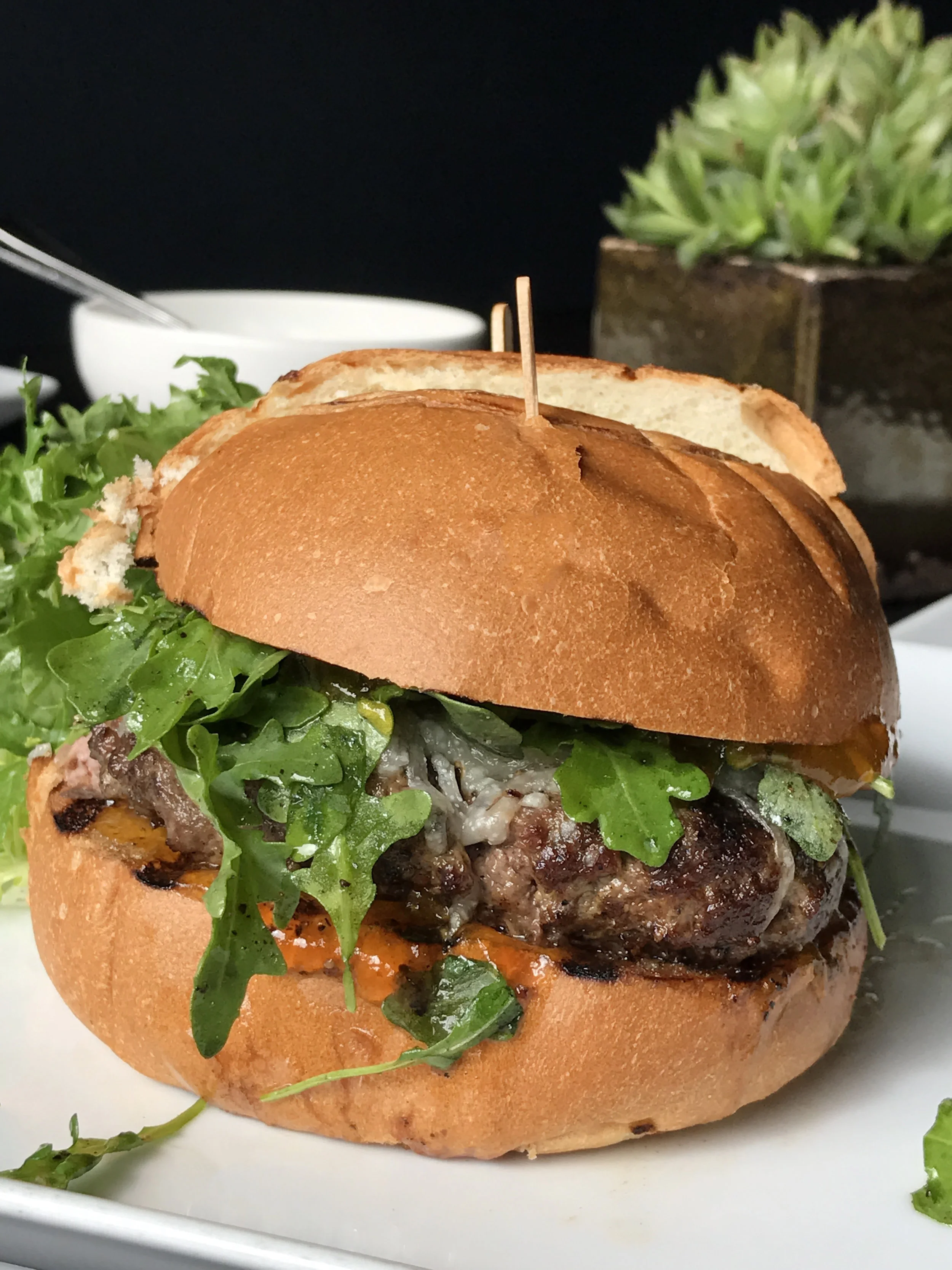 The Tripel Burger with duck confit, pork, and aged beef, arugula, truffle pecorino, house apricot jam, on an onion brioche