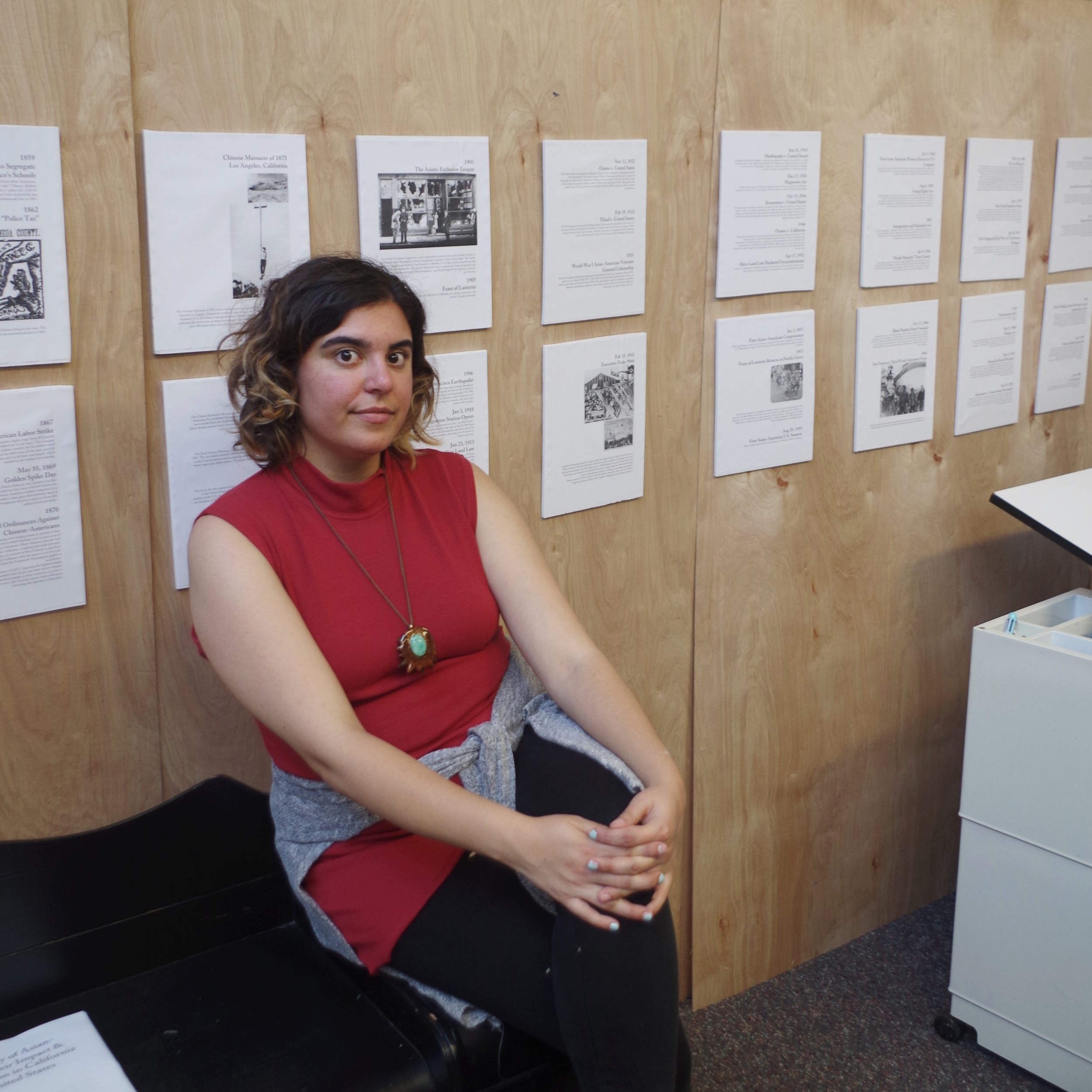 "Feast of Justice" - a history exhibition I put together as a protest of Feast of Lanterns. image description: the artist sits on her desk in front of the display, behind her is a timeline.