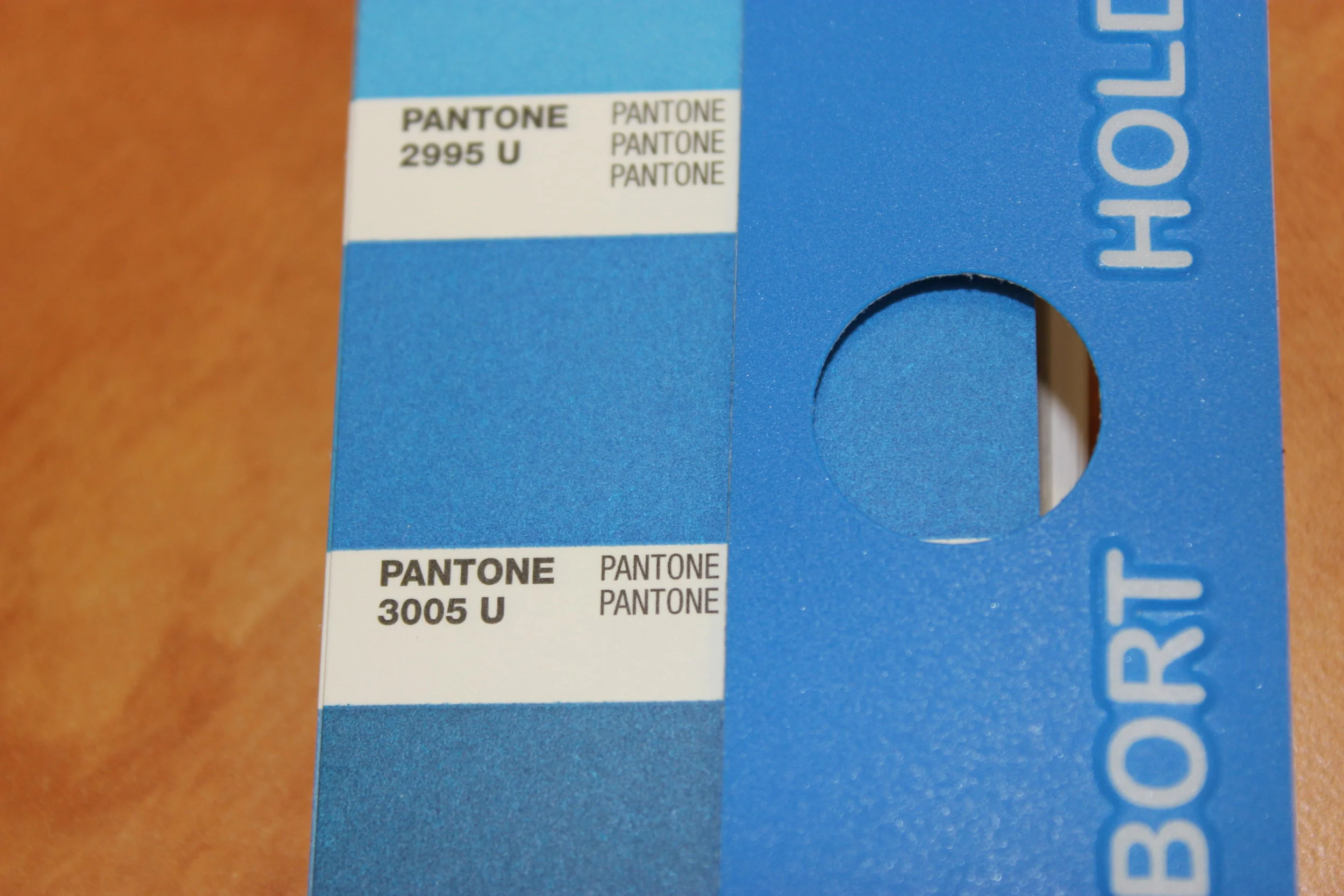 This Pantone booklet shows a matte finish, which was offset printed on paper, while the overlay uses the same color screen printed on plastic. To the trained eye, the colors are different - but still use the same formula. The cause for the difference in color: the material.