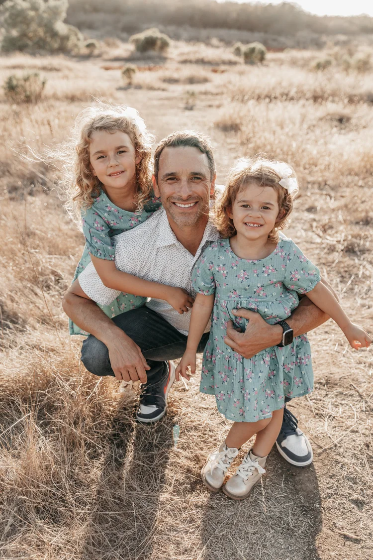 Ryan Danz, Air Concierge co-founder, crouching in a sunlit golden field with his two young daughters during a family stay at an Air Concierge home