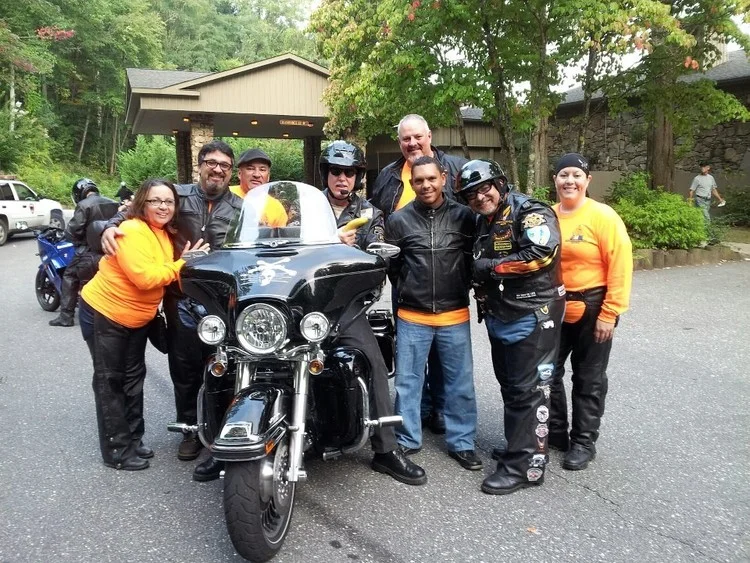 Pastor Tom Hughes sits on his Harley and AMM National President Juan Santos stands to the right wearing a helmet.