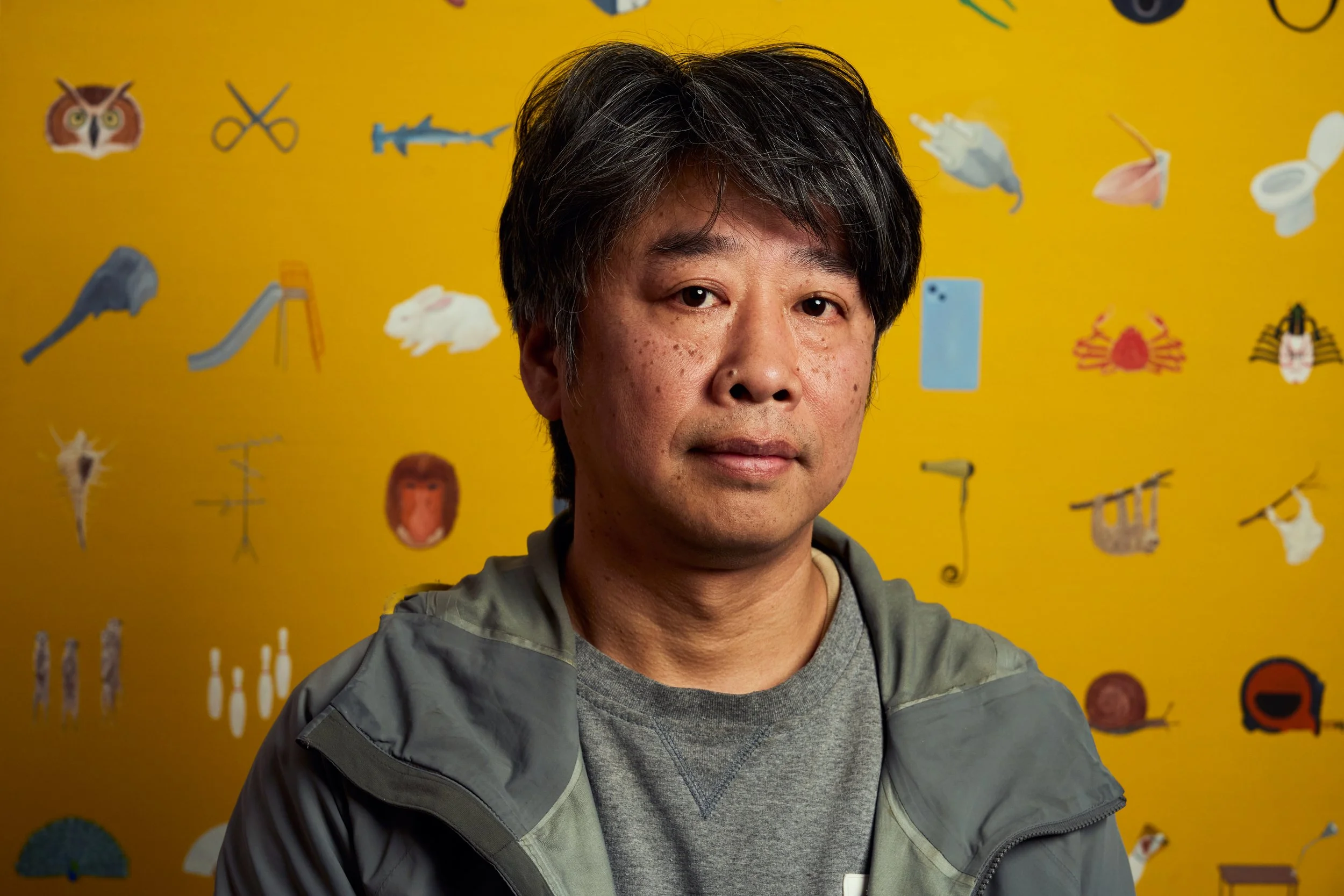 Editorial portrait of artist Akira Ikezoe in his studio before a canvas of small painted objects, photographed by Christopher Garcia Valle