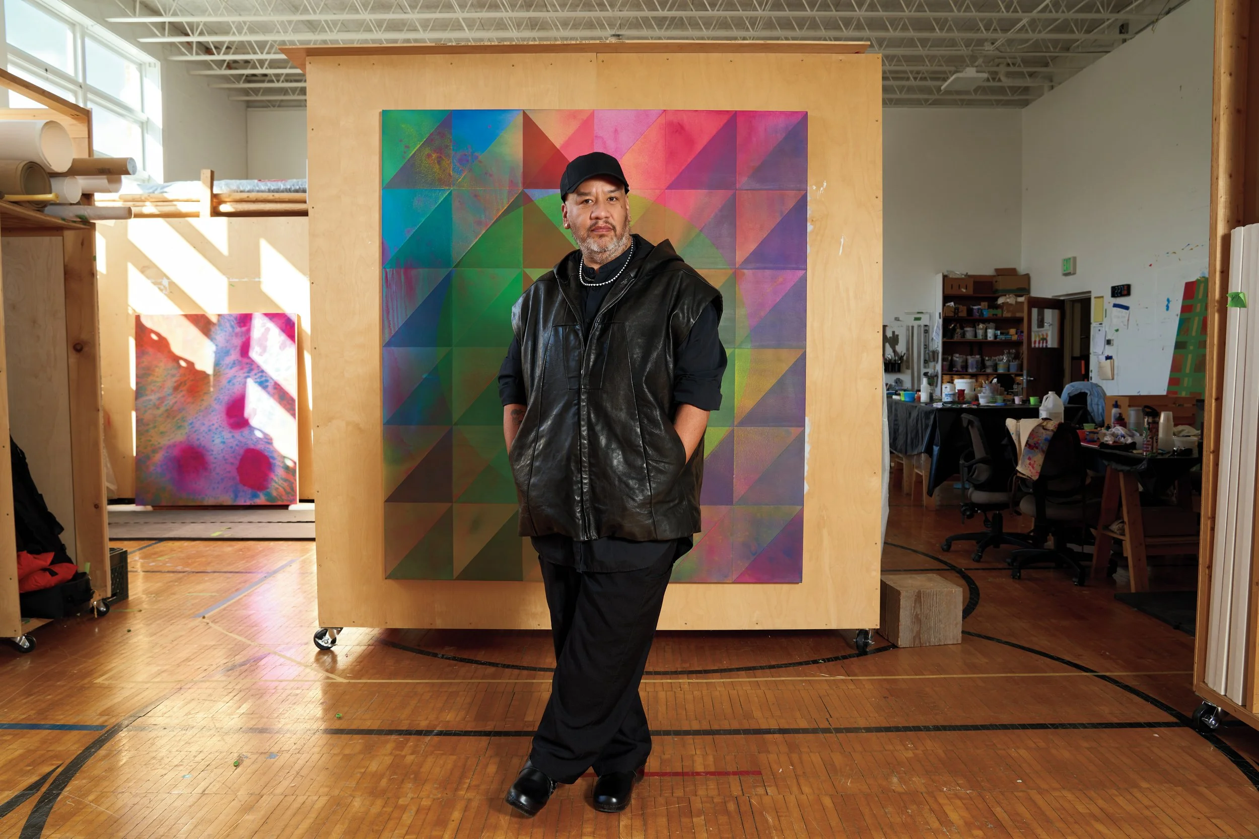 Editorial portrait of artist Jeffrey Gibson in his studio before one of his geometric color paintings, photographed by Christopher Garcia Valle