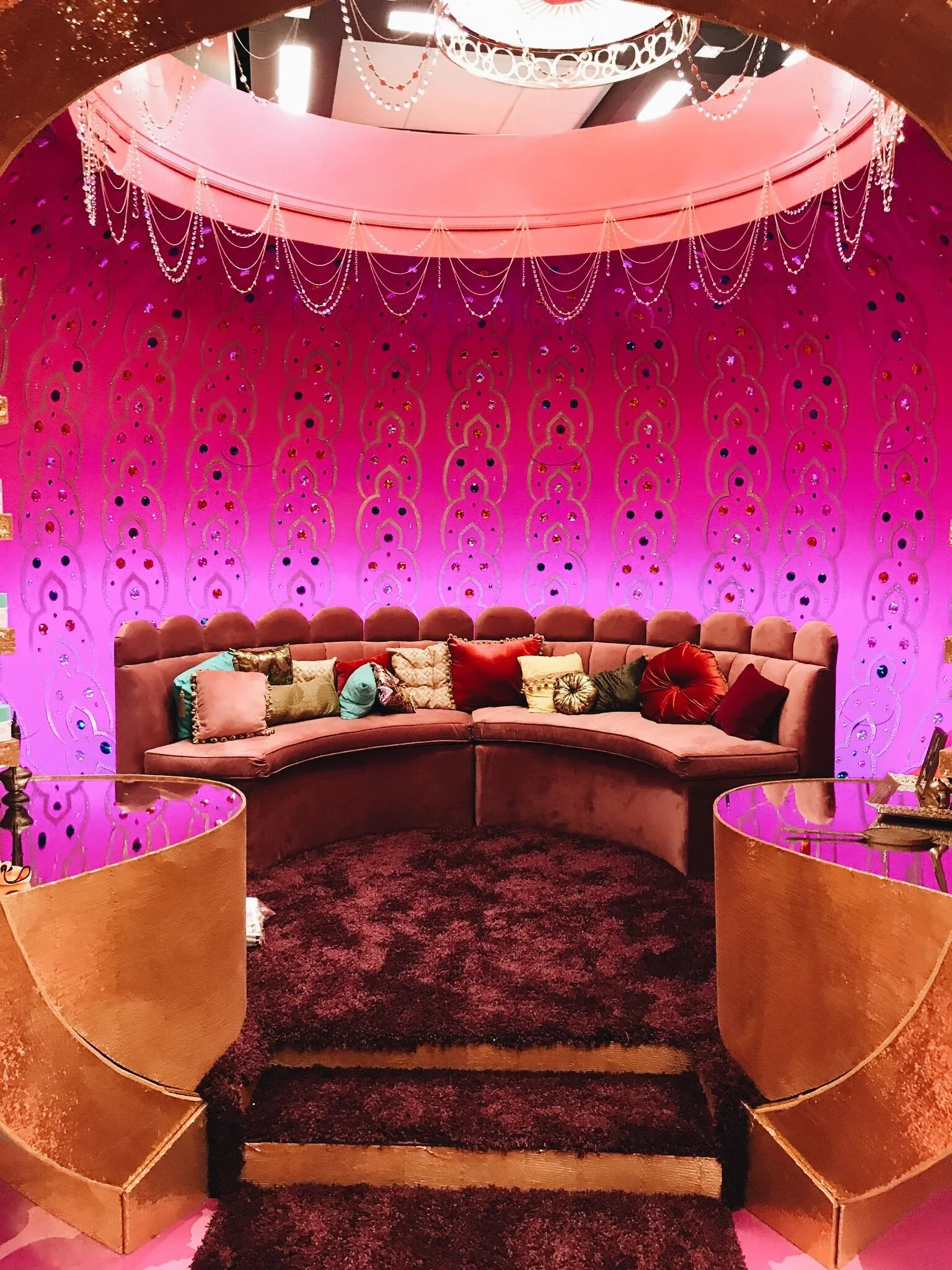 Custom pink lounge environment with scenic walls, chandelier detail, and branded event seating.