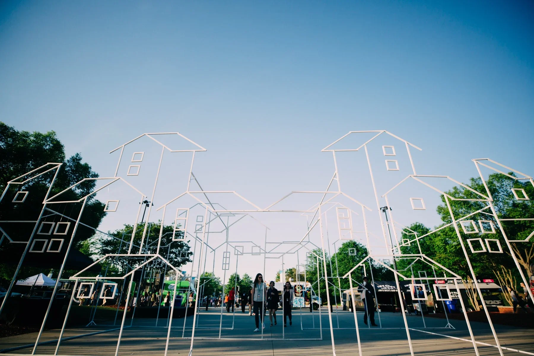 Large-scale outdoor neighborhood installation with wireframe house structures and immersive event layout.