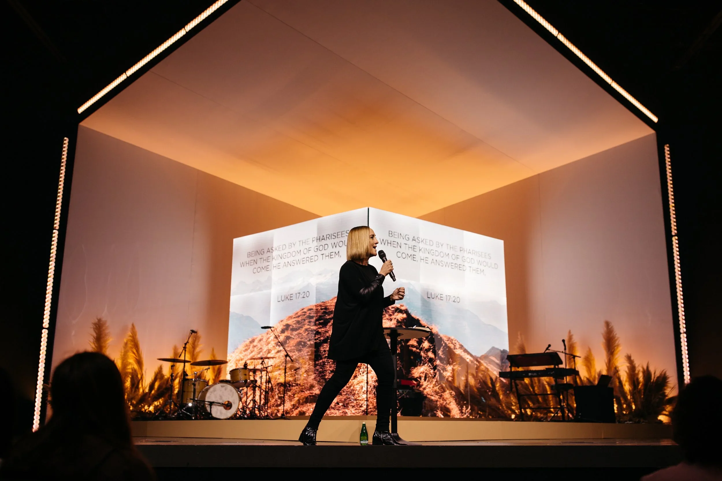 House-shaped scenic stage frame with projected landscape backdrop for a live event.