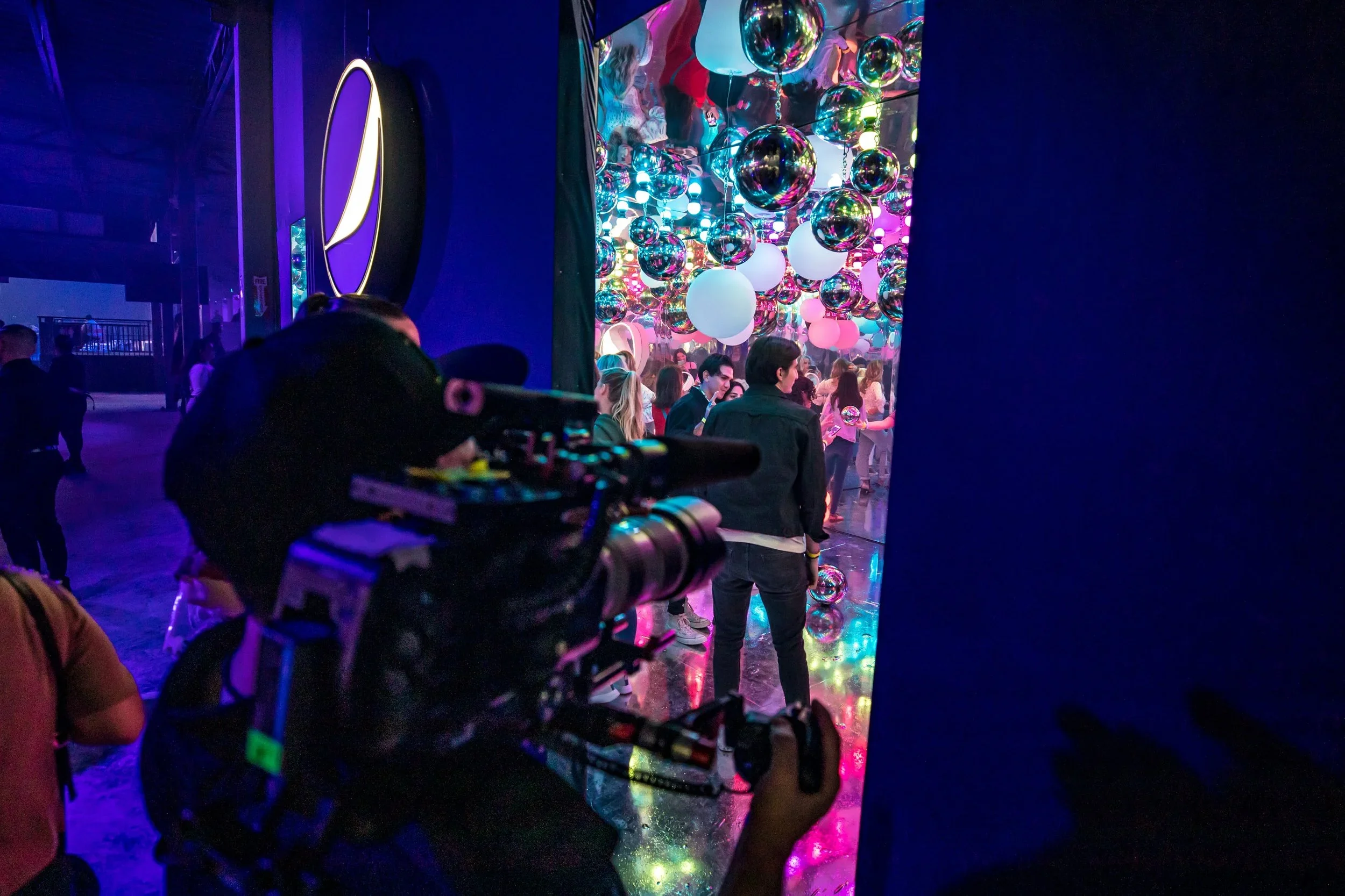 Immersive event installation with mirrored ceiling, hanging spheres, branded elements, and colorful lighting.