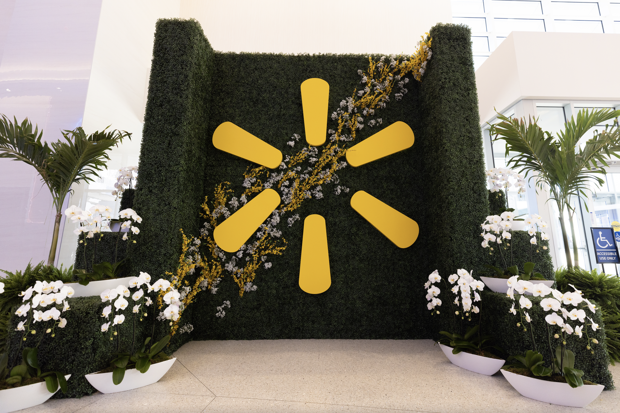 Custom greenery wall with dimensional logo elements, floral accents, and branded event display design.