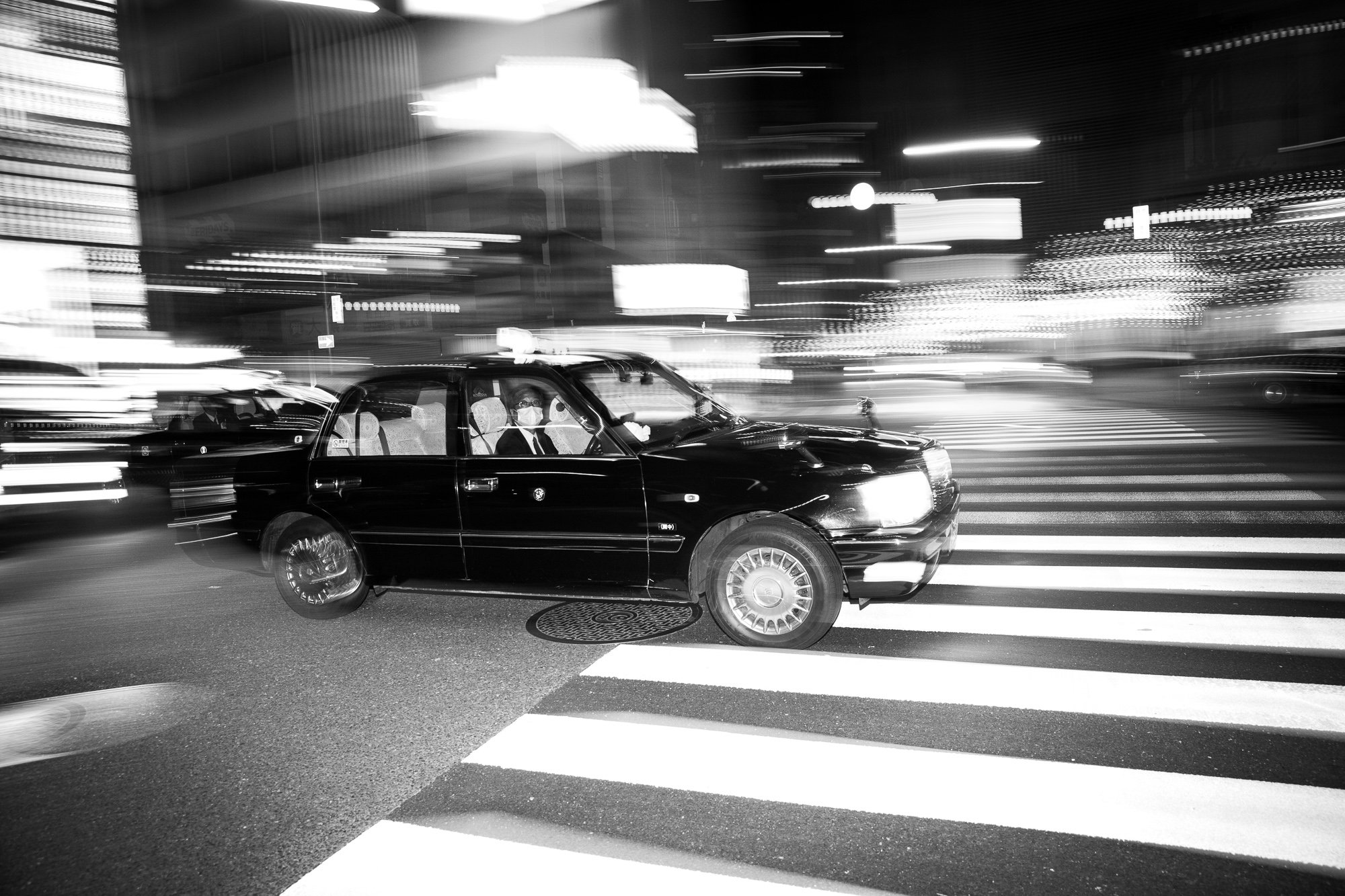 Black-and-white photograph of a taxi crossing a city street
