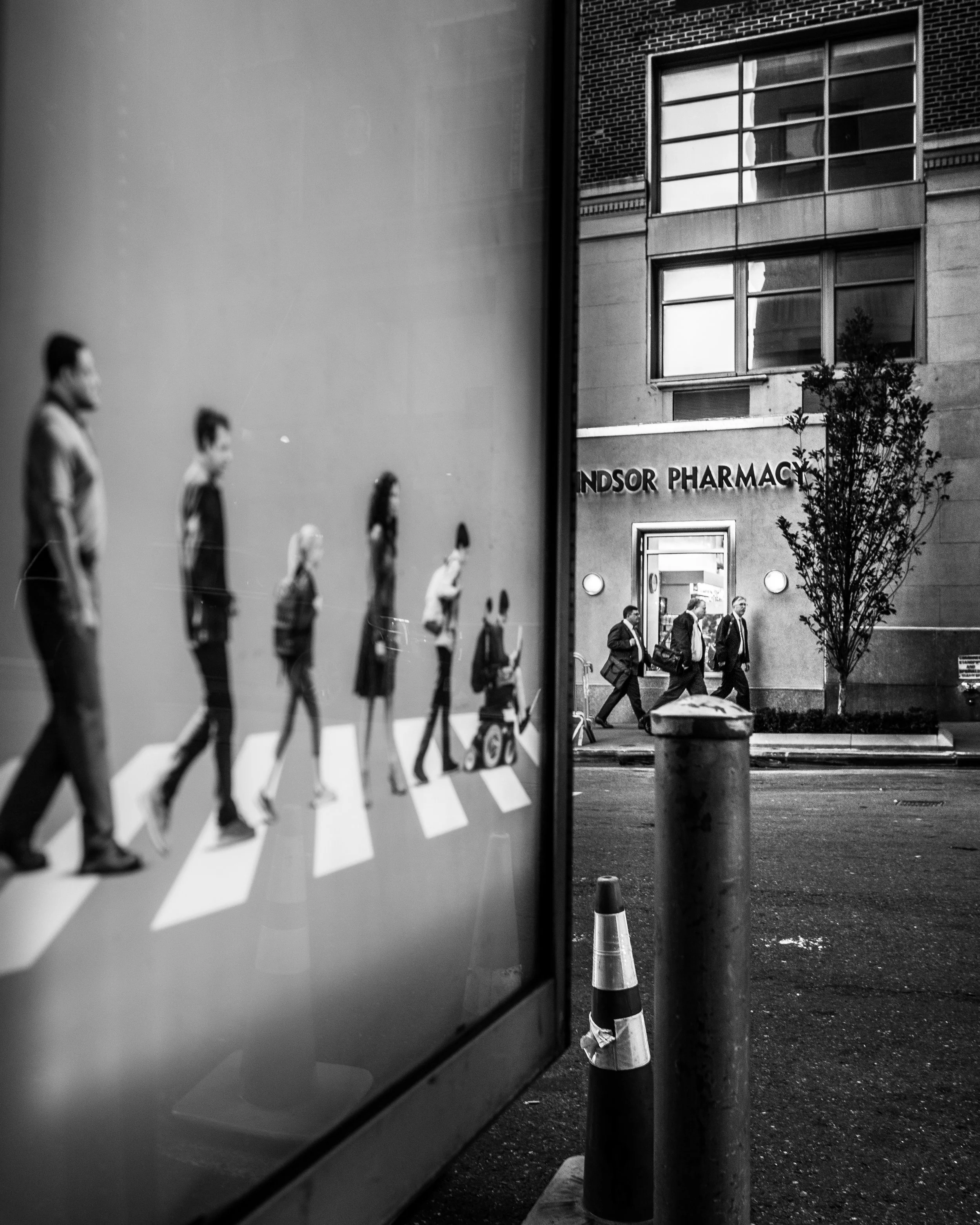 Black-and-white street photograph with reflected pedestrians