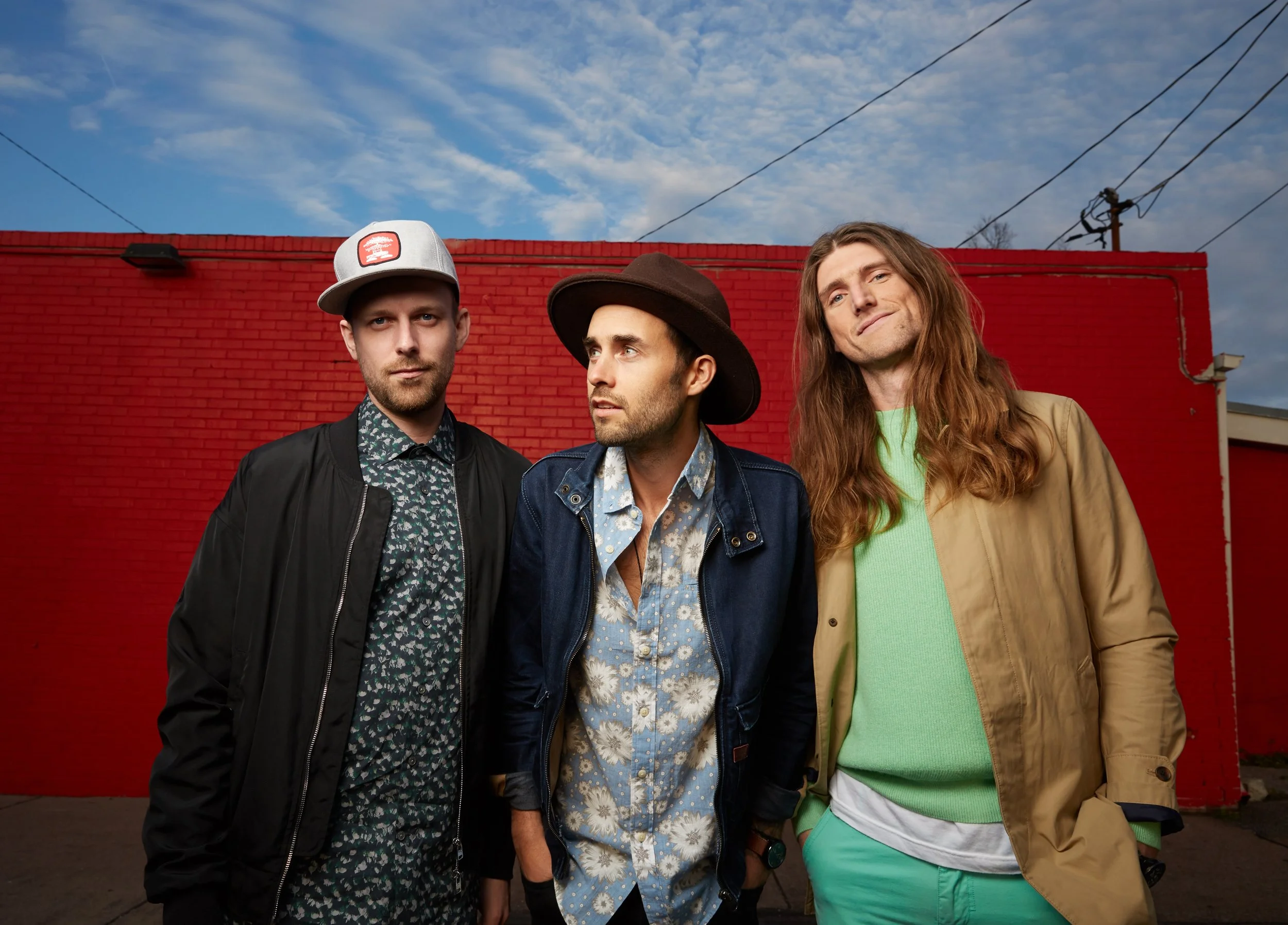 Three musicians photographed against a red wall