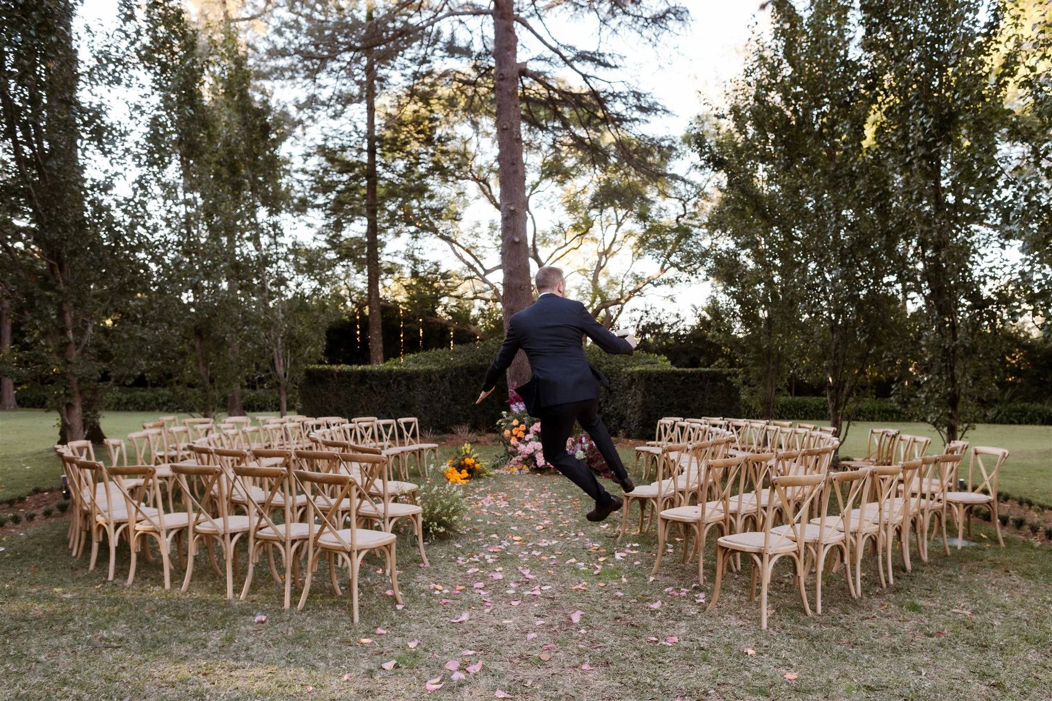 Gabbinbar wedding. A just married Groom leaping in the air with joy with a garden ceremony space in the background. Stories by Ash Photography