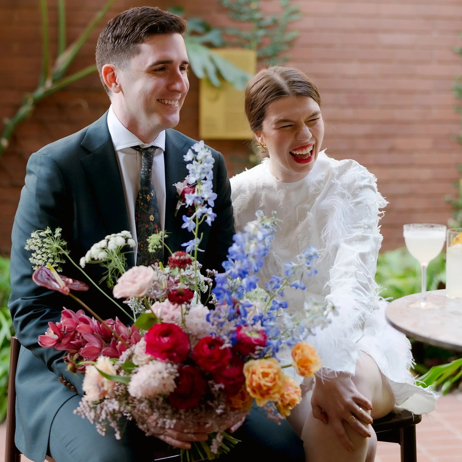 Happy couple laughing, holding a bunch of bright flowers. Stories by Ash Photography