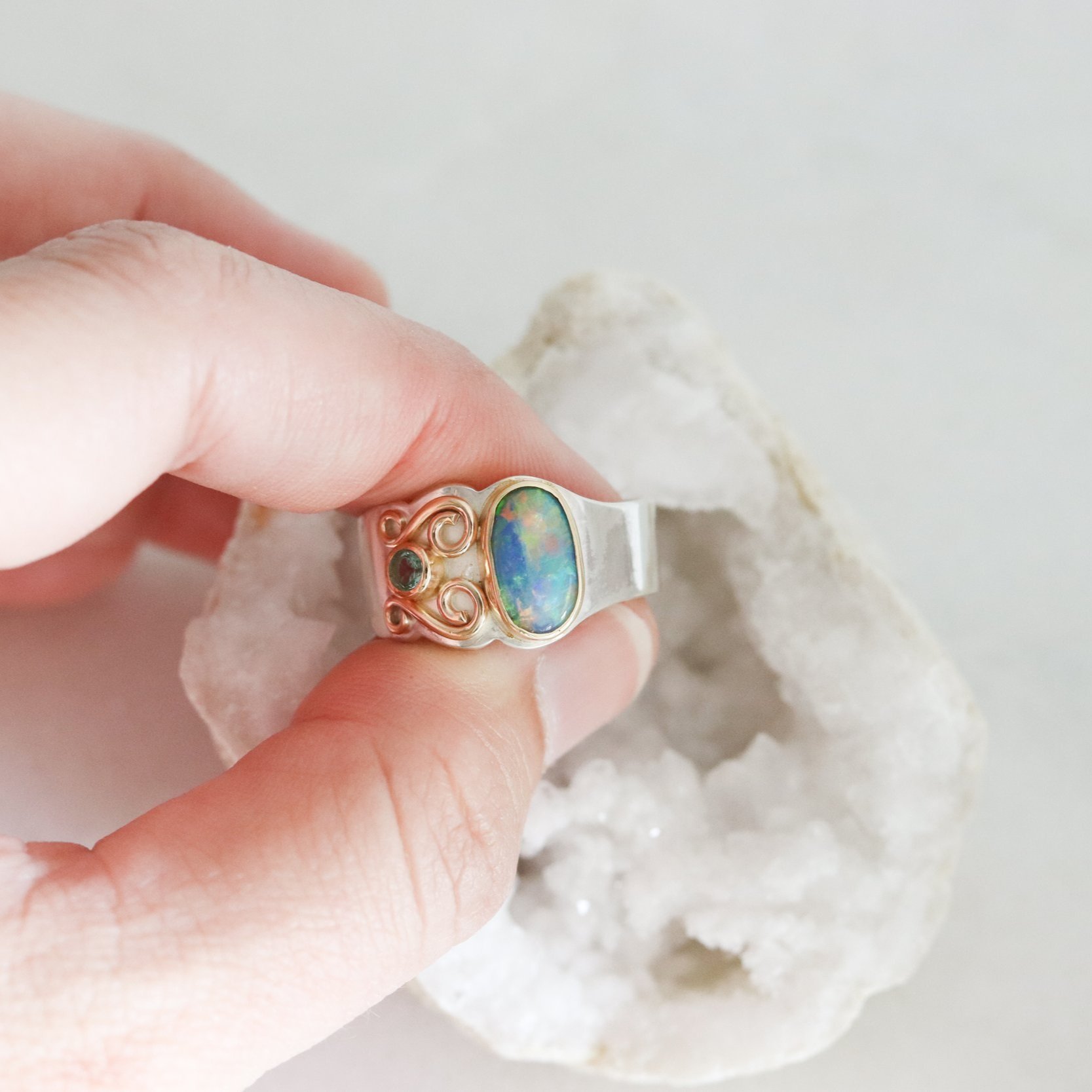 hand holding large opal ring over a geode