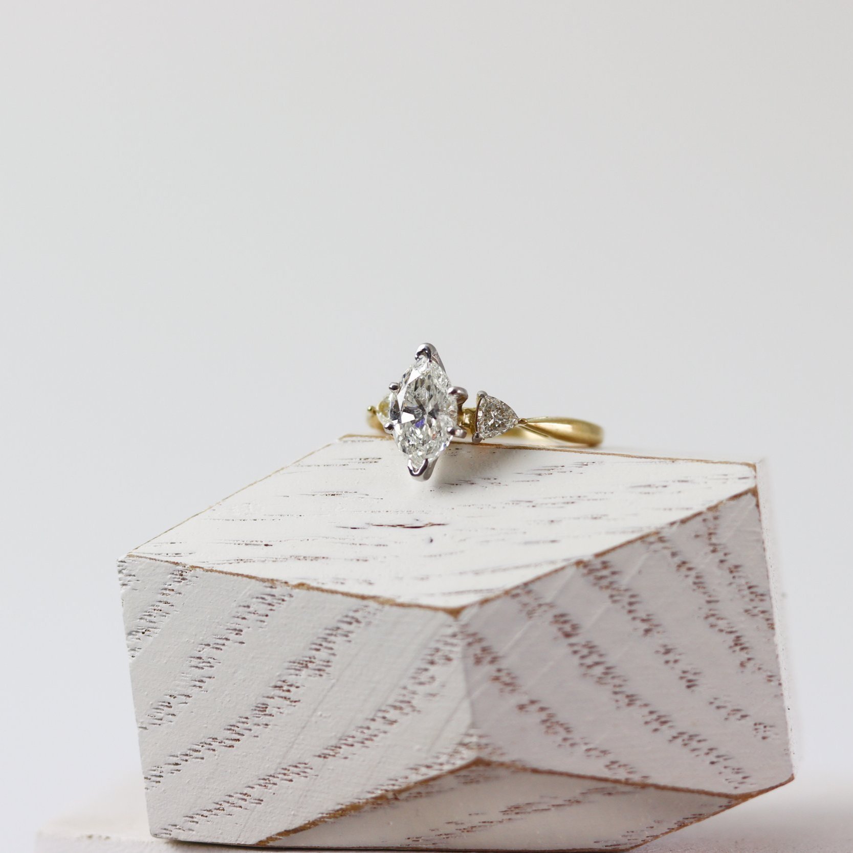 three stone engagement ring with marquise and trillion diamonds on a wooden block