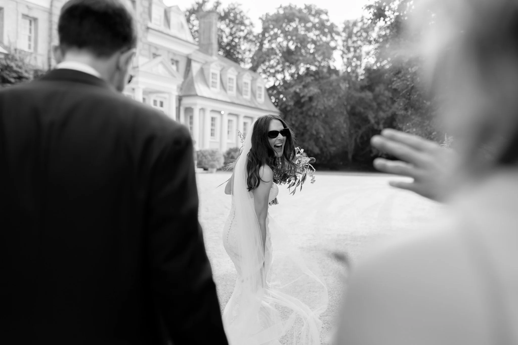 a bride turns back to look at guests, she is laughing. She wears sunglasses and the wedding venue is pylewell park in hampshire