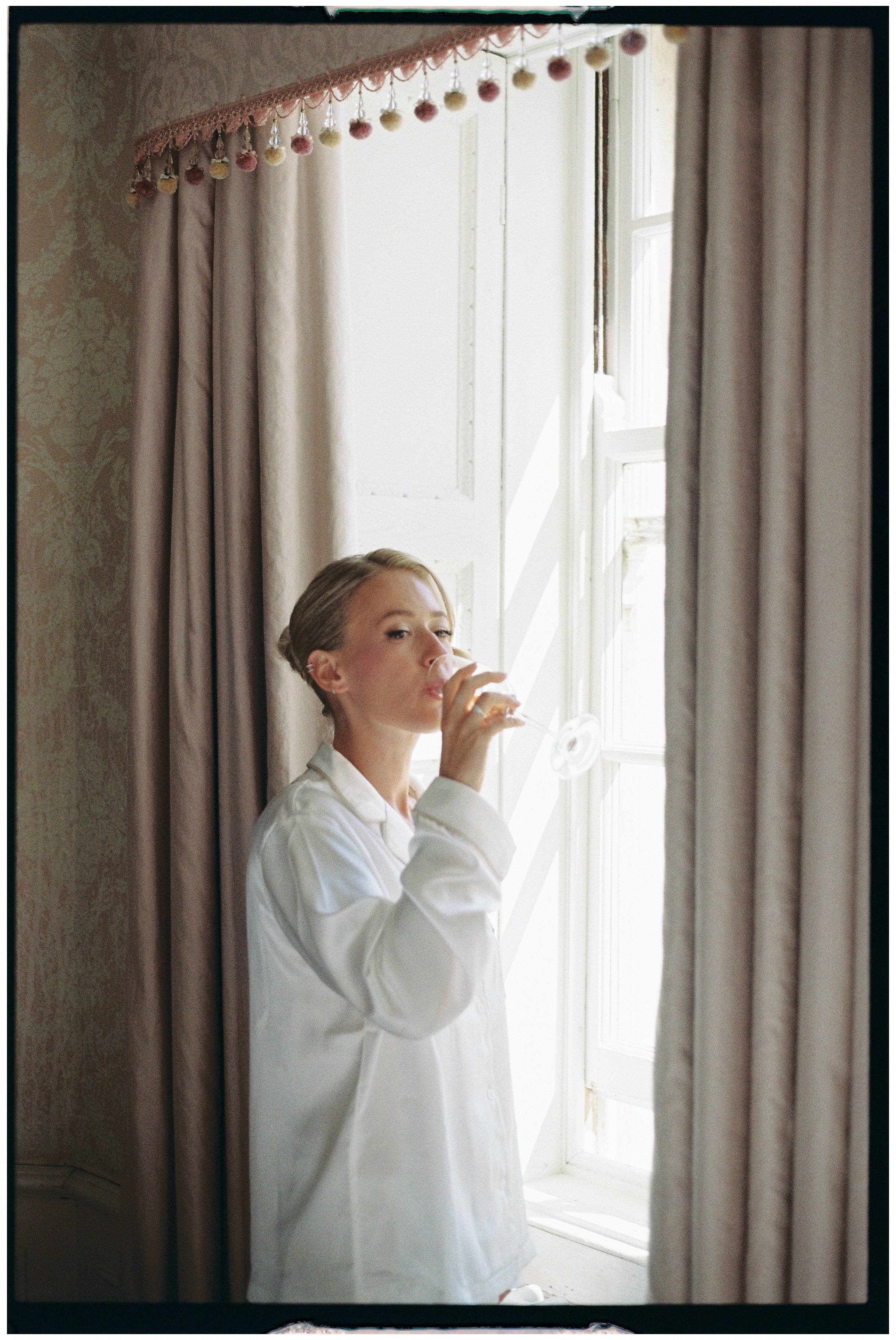a film image of a bride looking out of the window drinking champagne