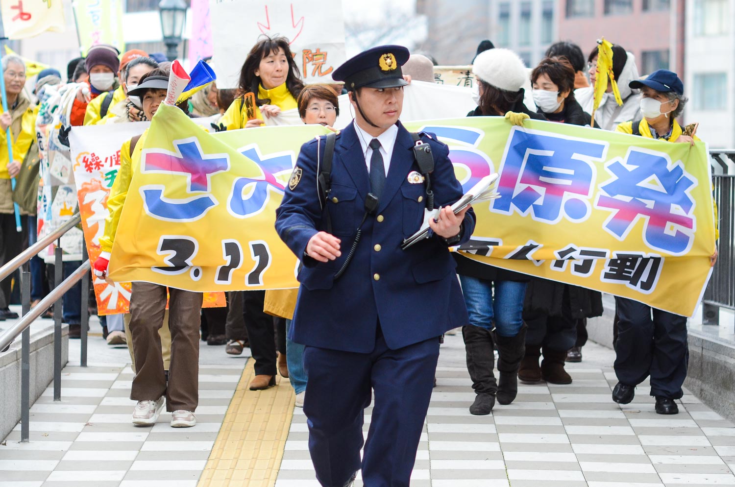  A police officer leads a group of people protesting against the use of nuclear power in Japan. 