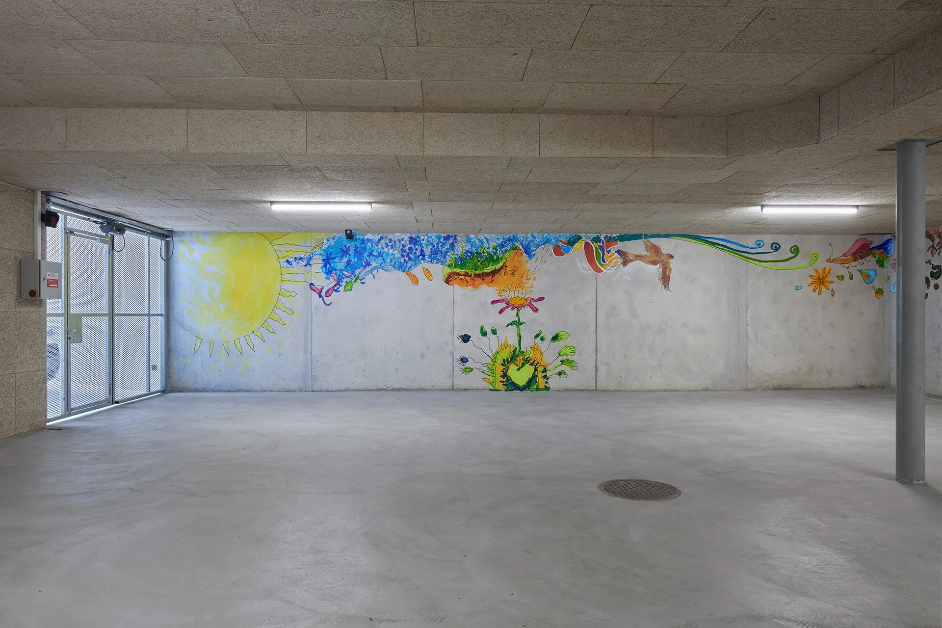 An empty concrete passage features a colorful mural of a radiant sun, flowers, and flowing shapes along the back wall, brightening the stark space.