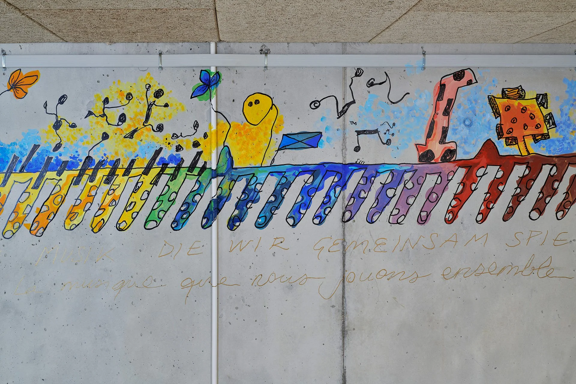 Colorful children’s mural of a yellow duck, butterflies, playful figures, and rainbow-striped shapes on a concrete wall, conveying a cheerful, imaginative mood.