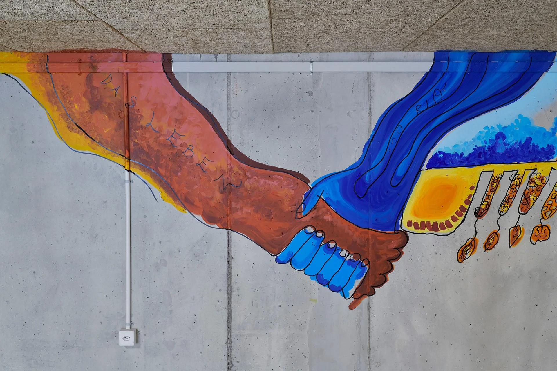 A colorful mural on a concrete wall shows two hands clasping across a gap, their patterned sleeves in warm red and cool blue, symbolizing unity.