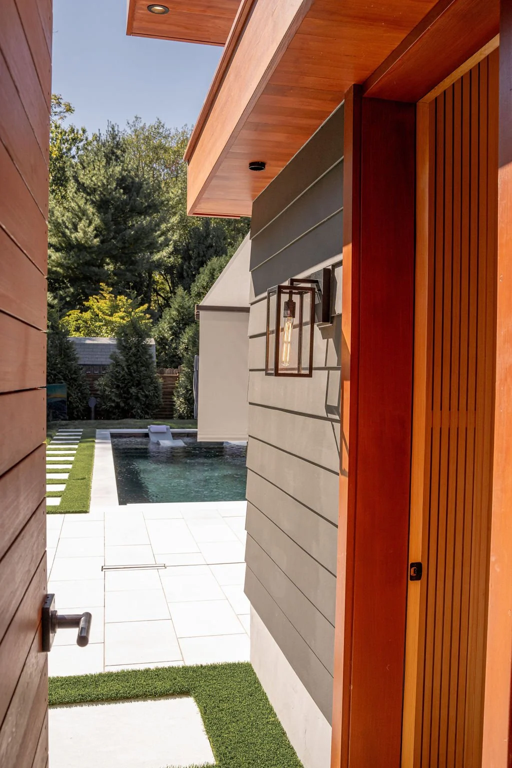 View from an open door looking towards a backyard with a swimming pool, green trees, and a blue sky.