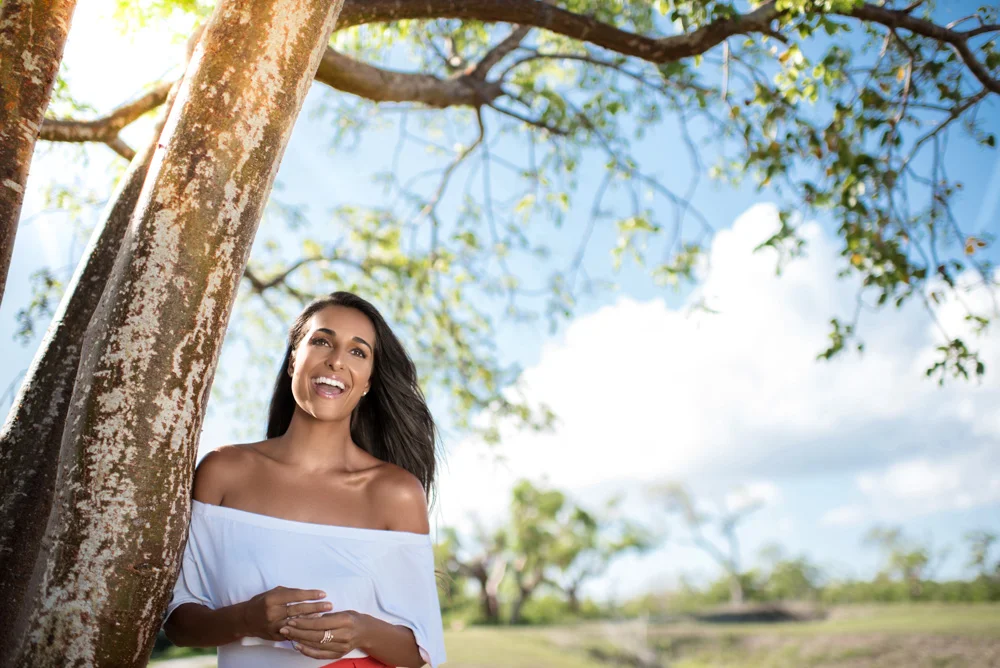 This is a portrait of a young spanish woman laughing under a tree.