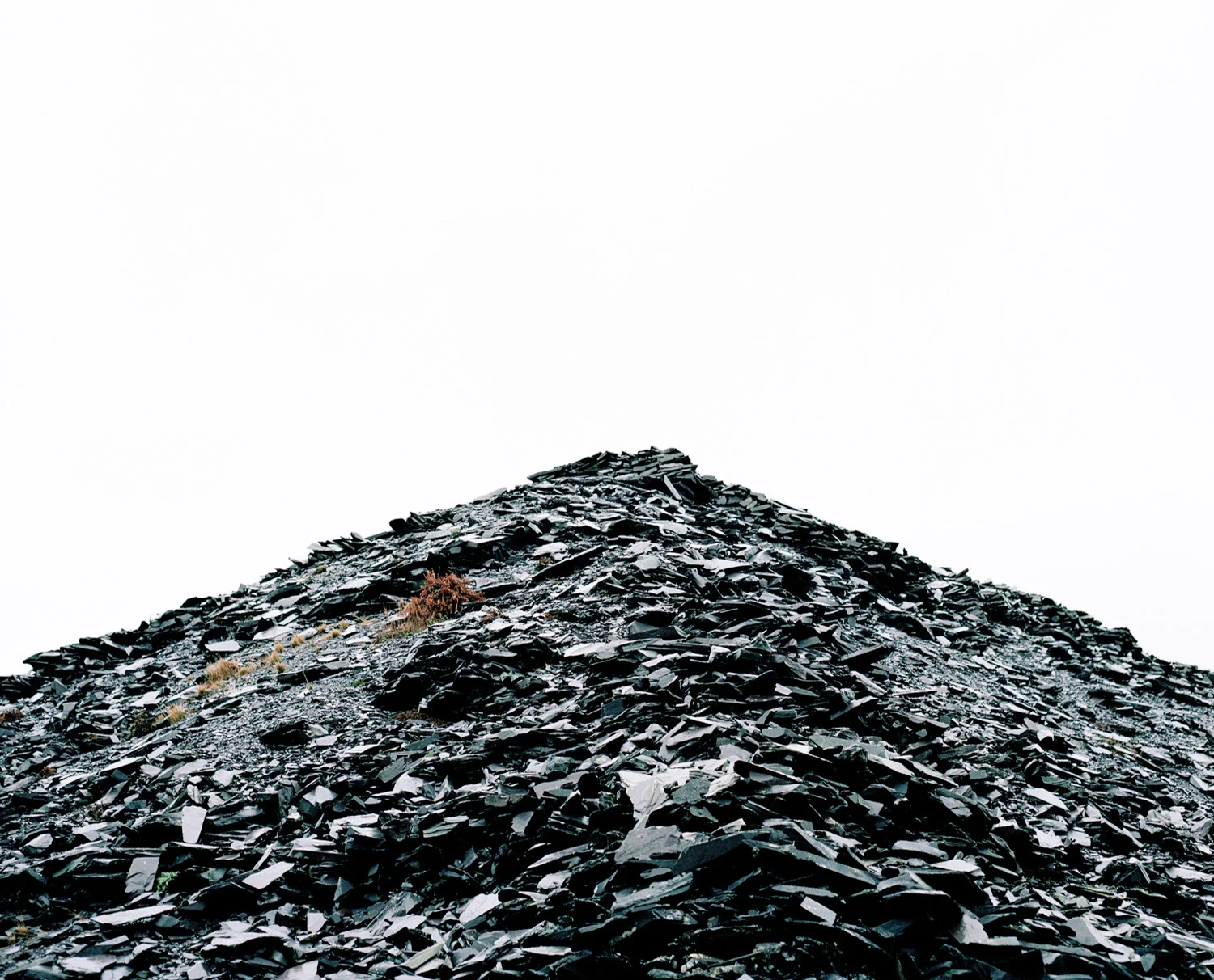 A large pile of black slate shingles forming a mound against a white sky.