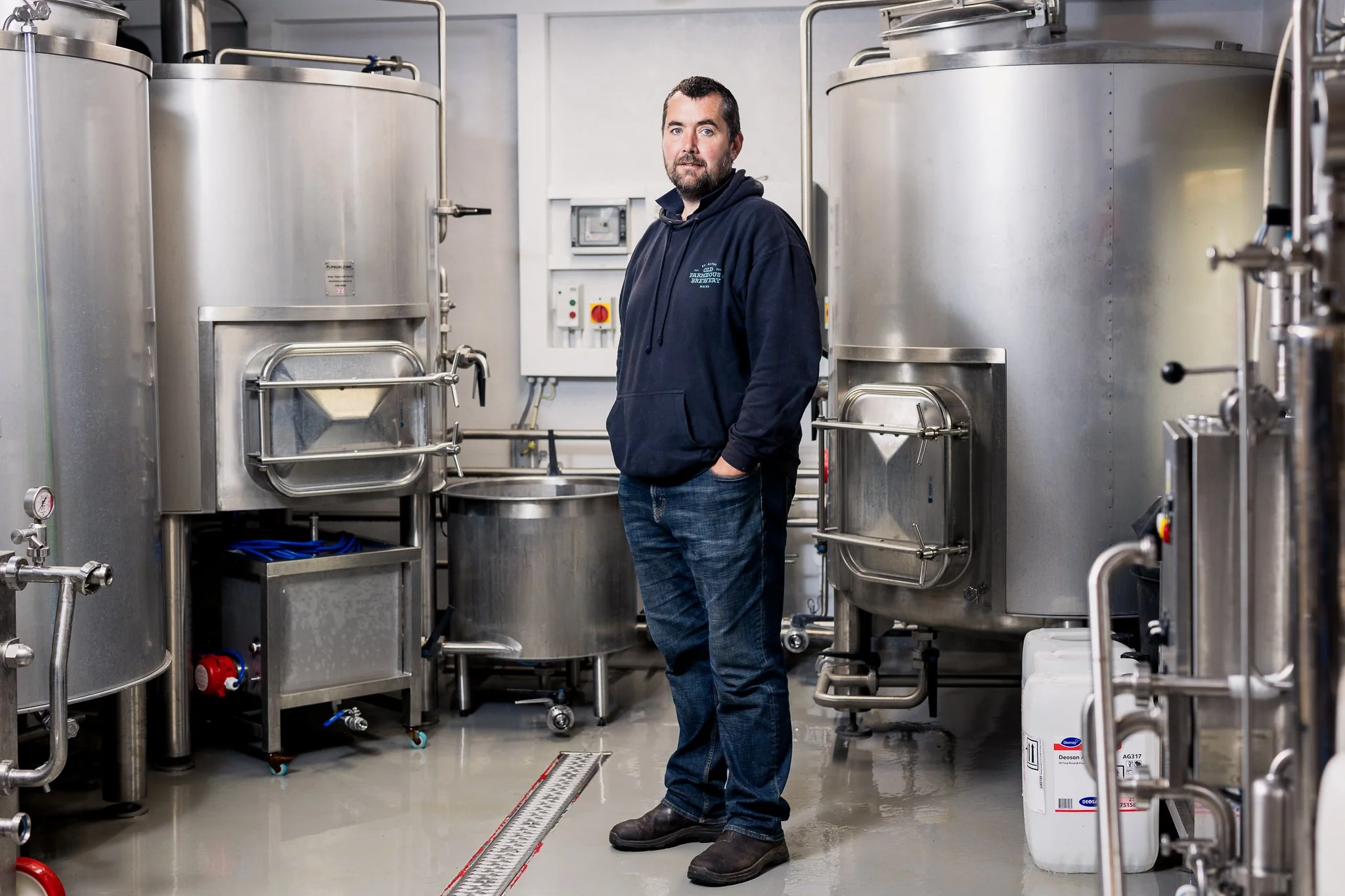 A man standing in a brewery with stainless steel fermentation tanks surrounding him.