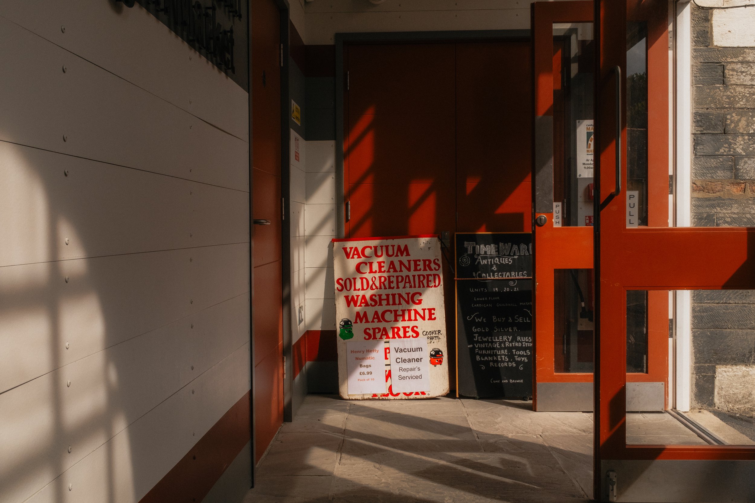 Storefront entrance with signs advertising vacuum cleaners, repair services, collectibles, jewelry, rugs, furniture, tools, and toys.