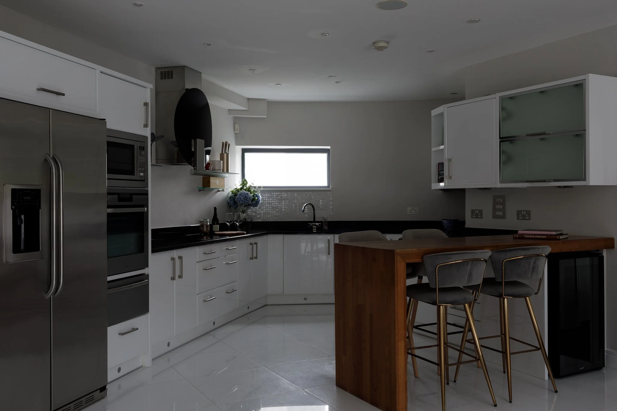 Modern kitchen with white cabinets, stainless steel refrigerator, black countertop, and a wooden breakfast bar with four chairs.
