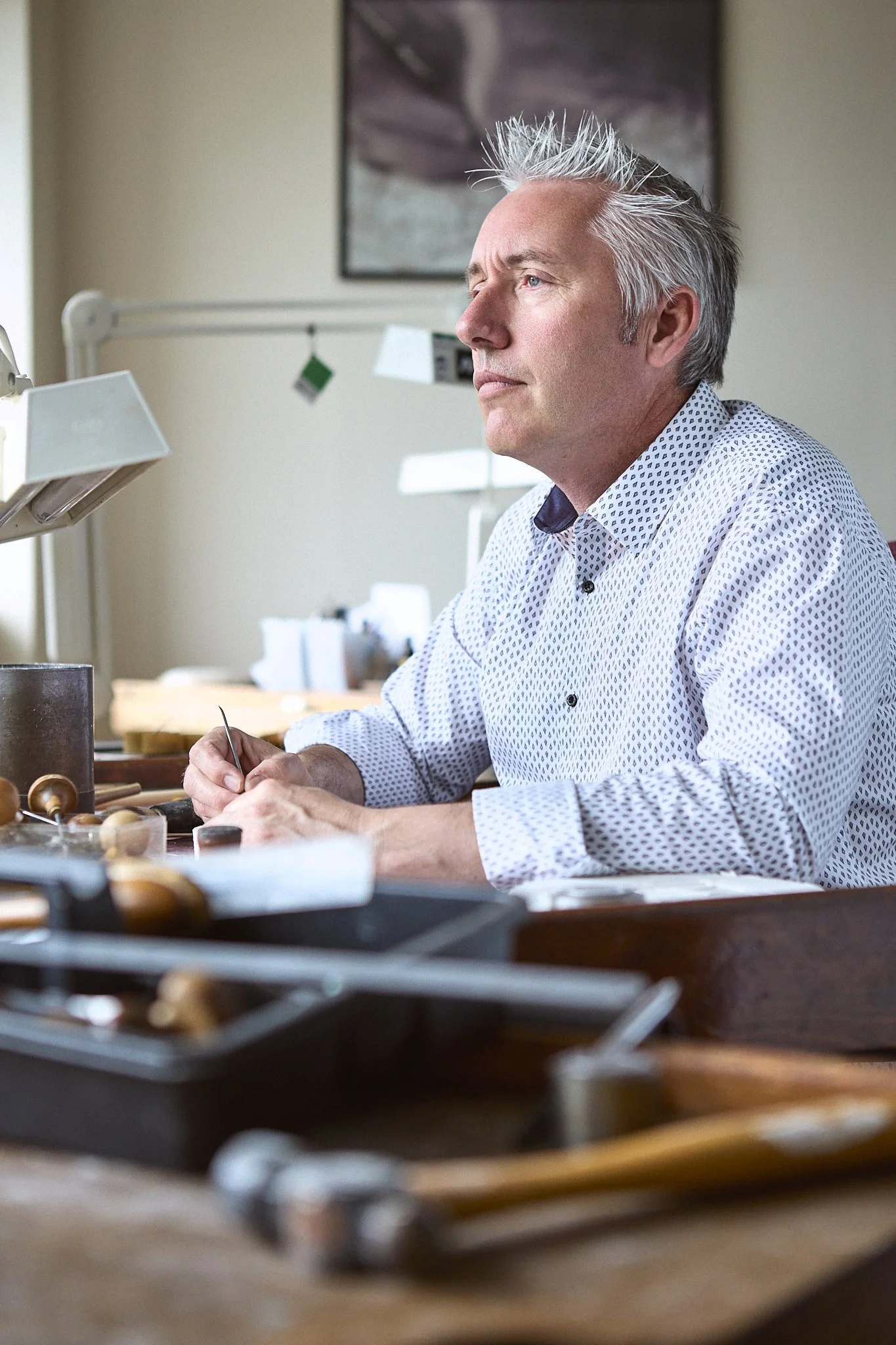 A mature man with gray hair working at a jewelry bench, focusing intently on his craft.