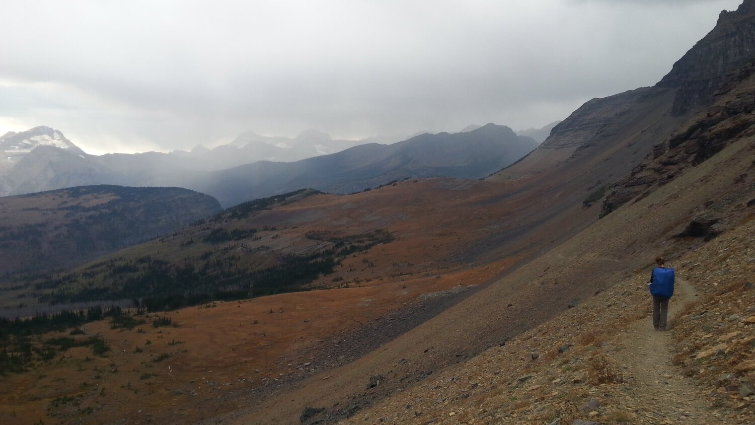A hiker on a rocky trail in Glacier National Park with misty mountains in the distance