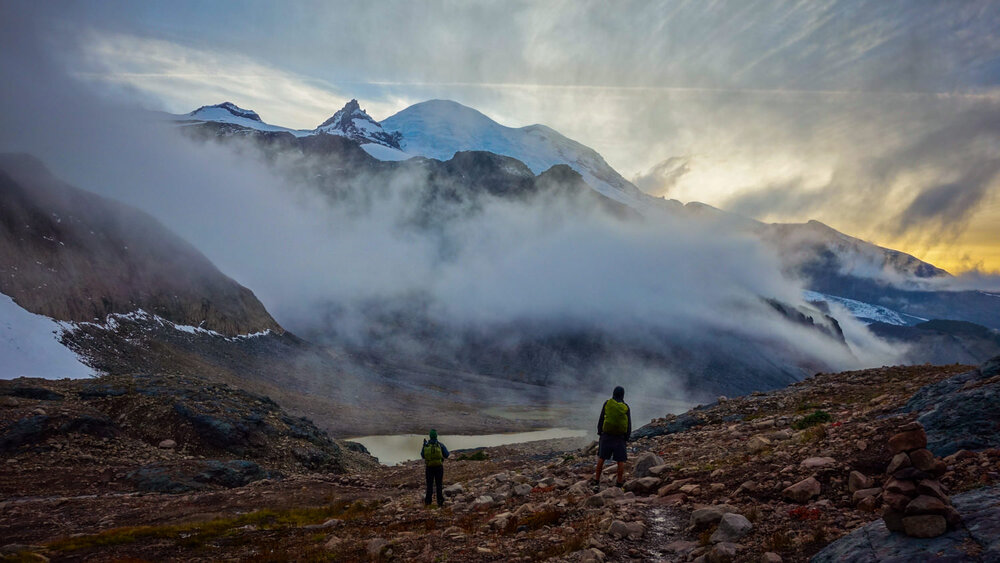 Two backpackers standing in front of a foggy mountain view