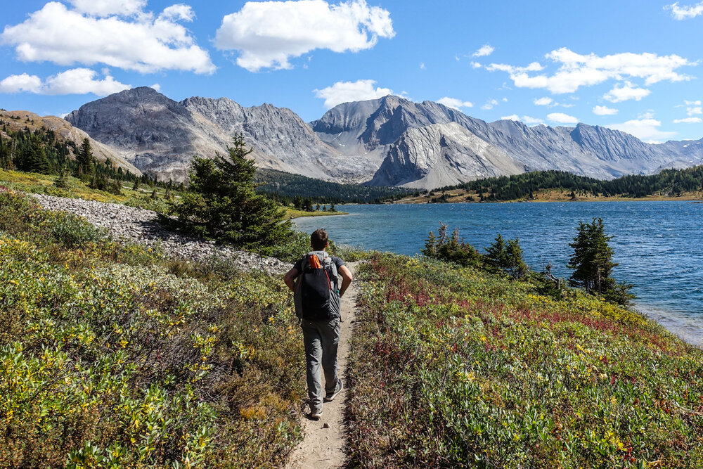 A backpacker hiking on a trail next to a lake with mountains in the distance