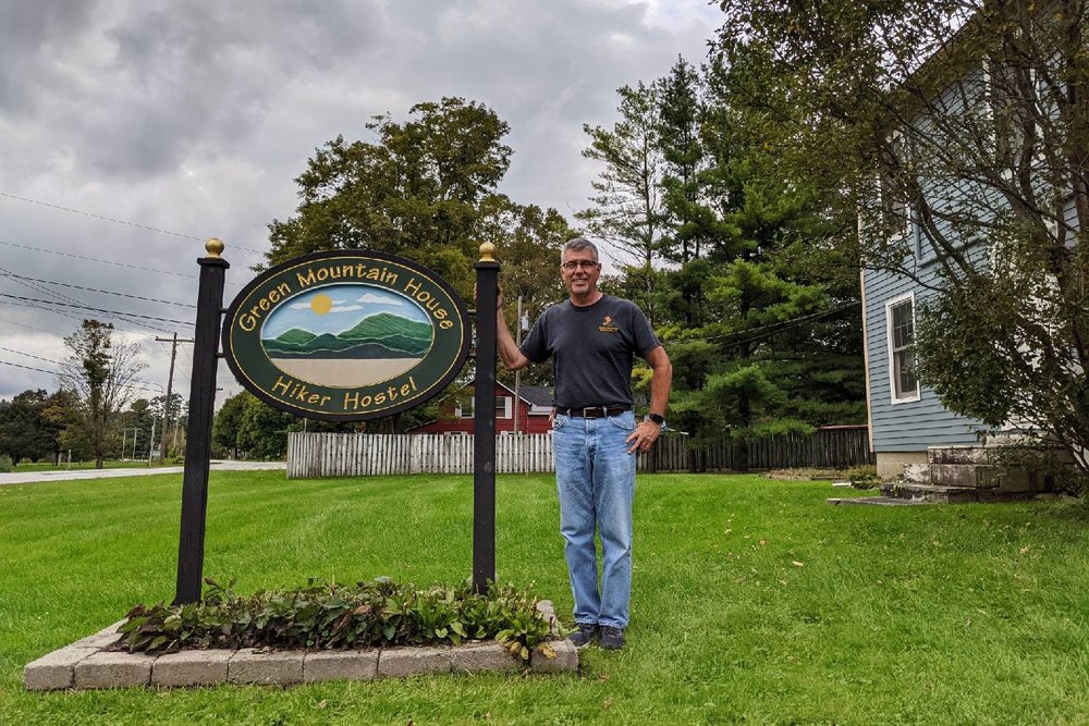 Owner Jeff Taussig standing next to the Green Mountain House Hiker Hostel sign
