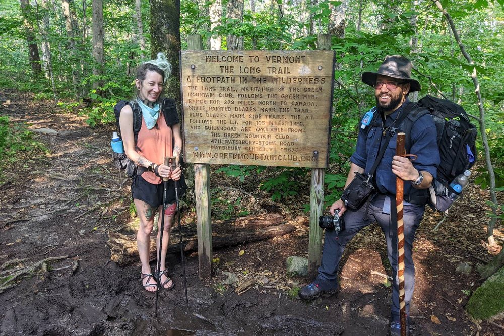 Two hikers standing next to the Long Trail southern terminus sign