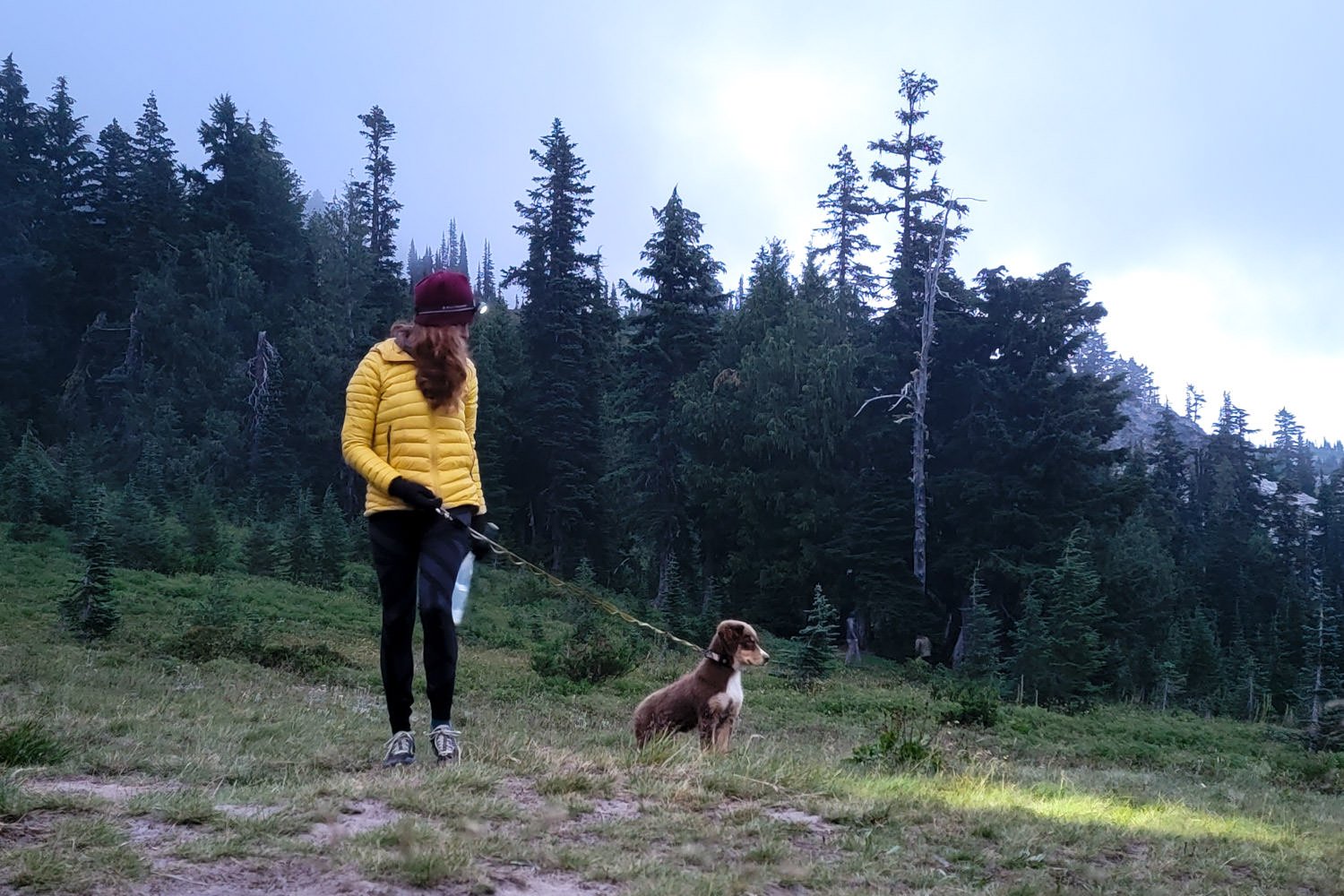 Un excursionista con un faro paseando a un perro por un sendero al atardecer