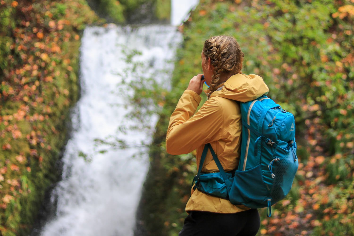 Un excursionista bebiendo de un paquete de hidratación frente a una cascada