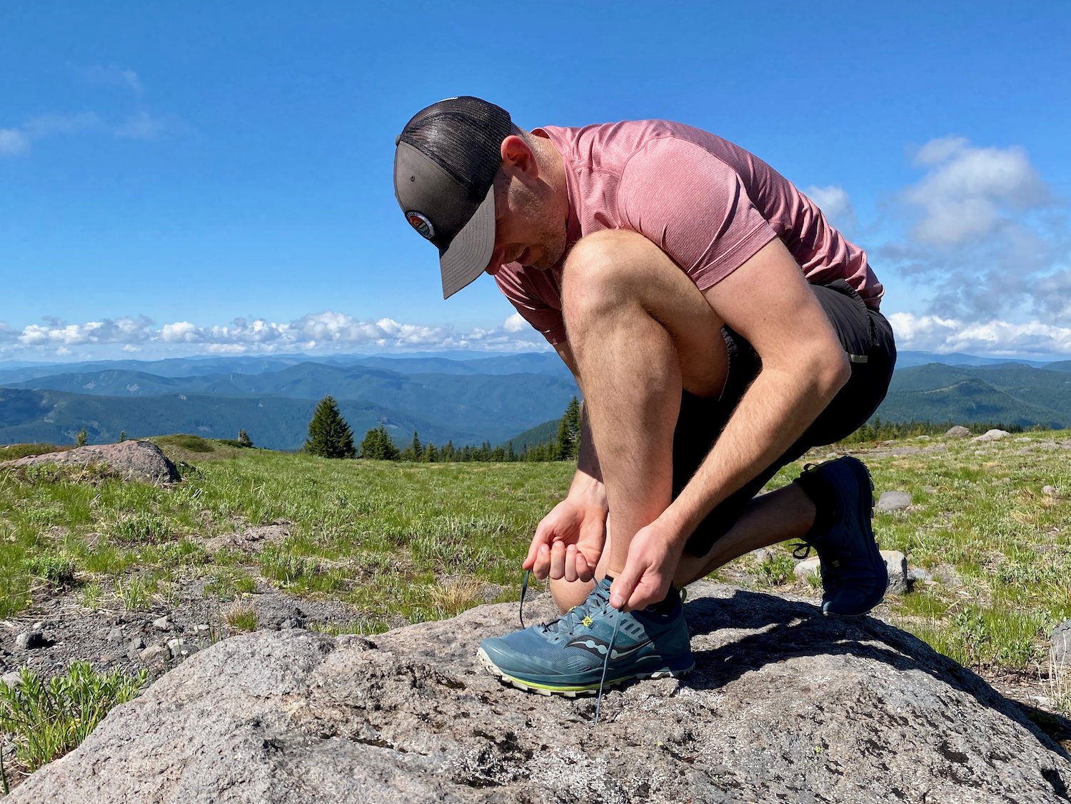 Un excursionista atándose el zapato con una amplia vista del valle al fondo